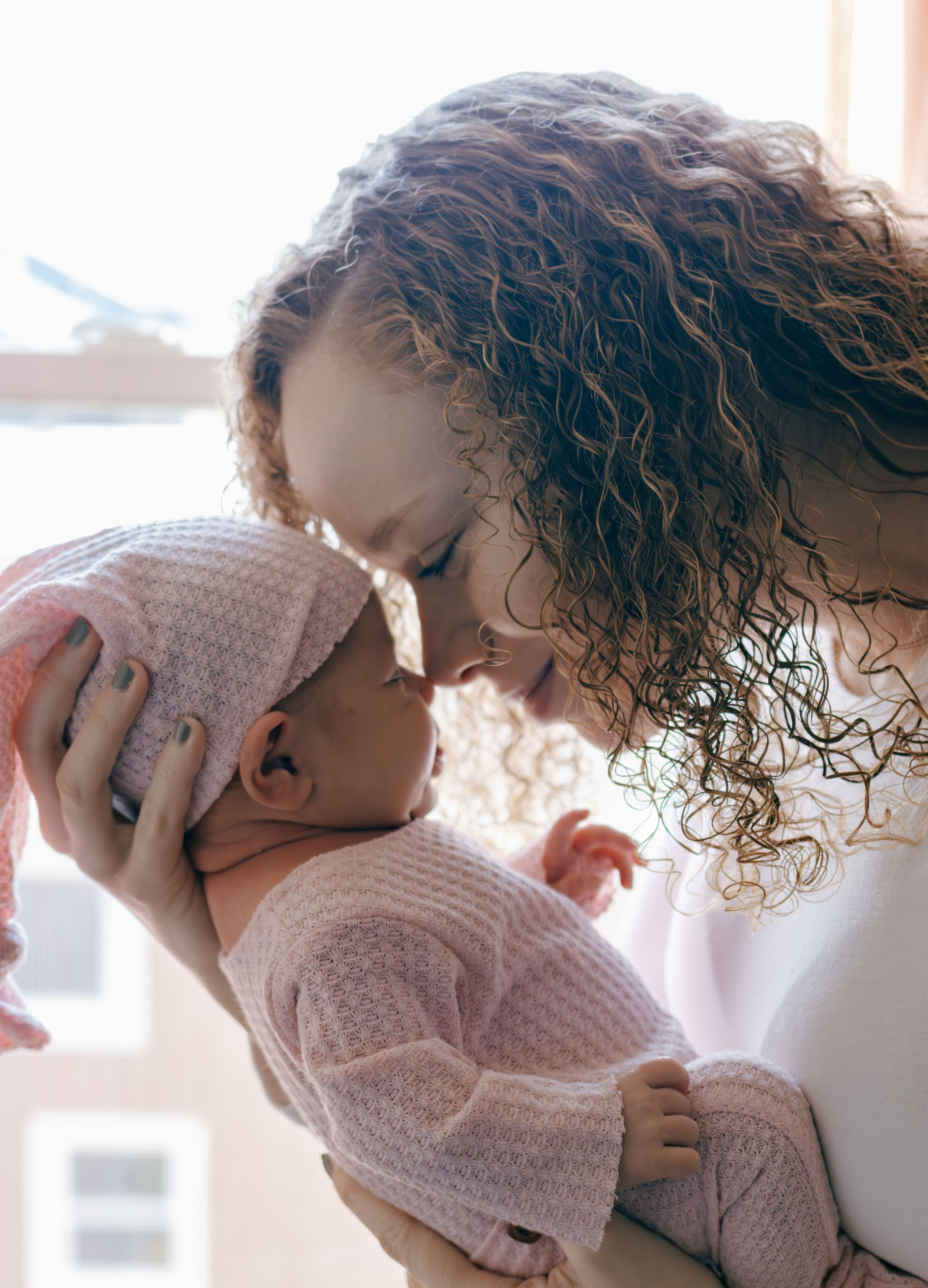 Sunlit portrait of caregiver cradling baby in gentle embrace.