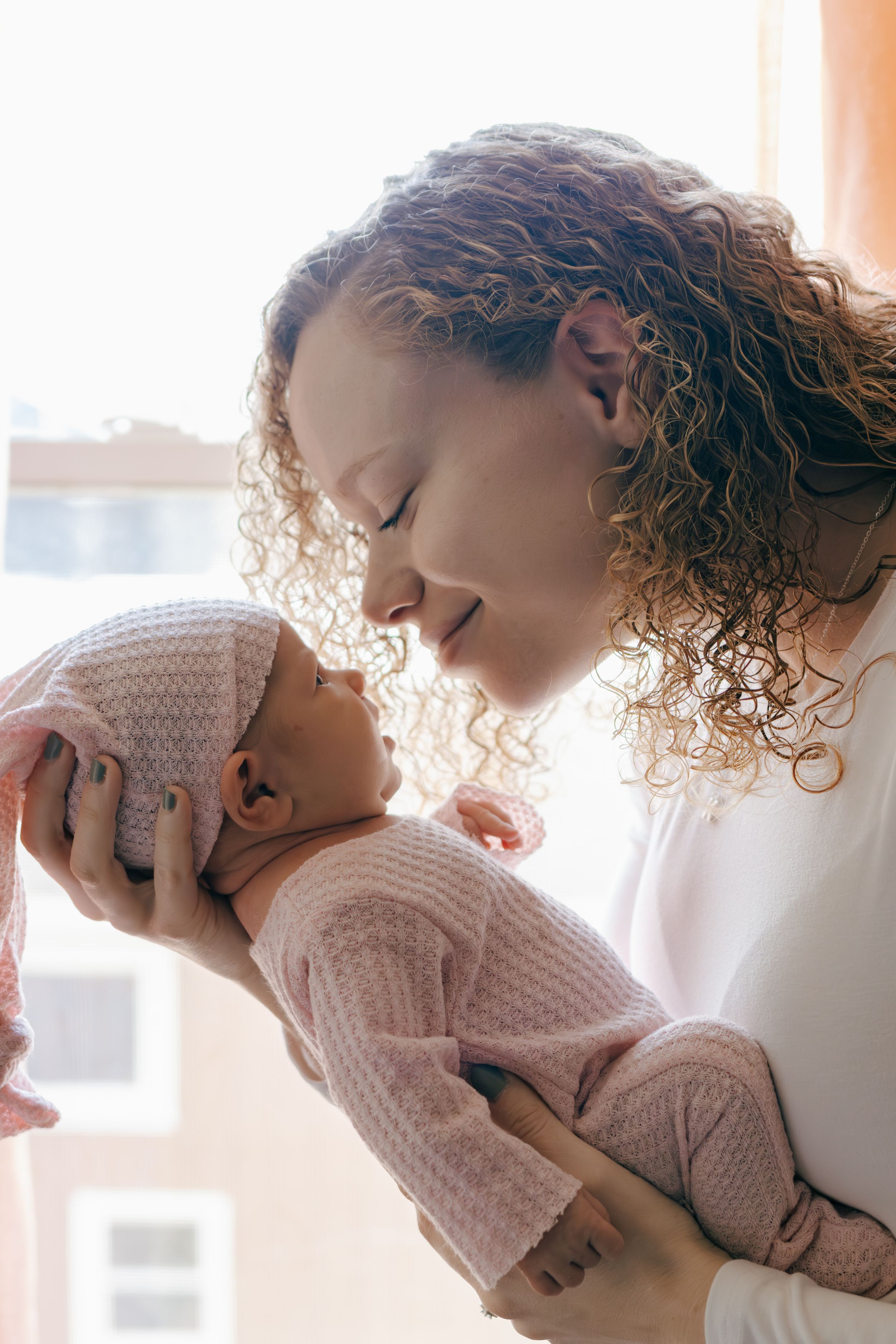 A tender moment between parent and infant wearing pink knit clothing in soft window light.