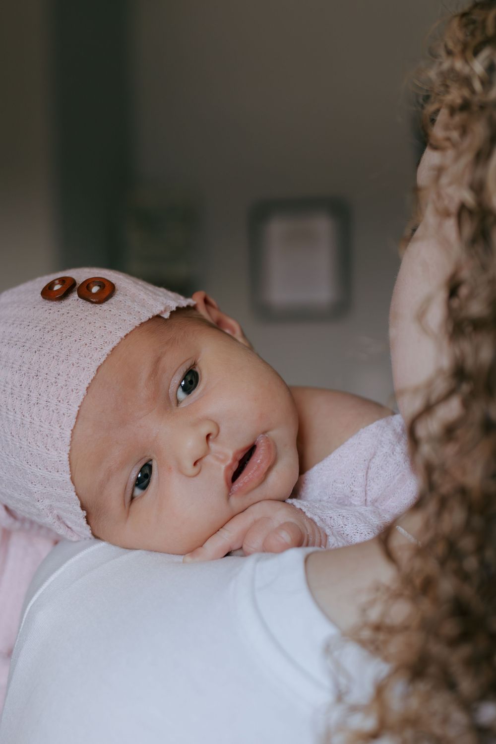 Baby in white knit outfit with brown buttons gazes up with bright eyes.