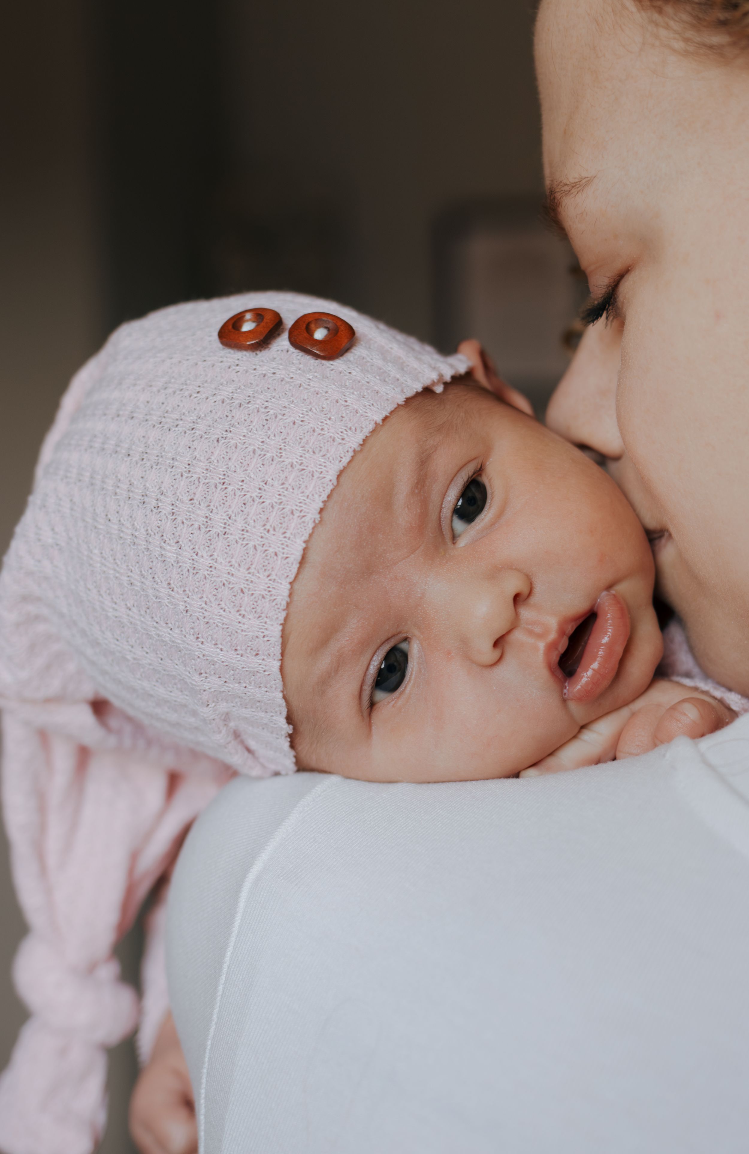 Newborn in pink knit clothing with decorative buttons looks alert and curious.