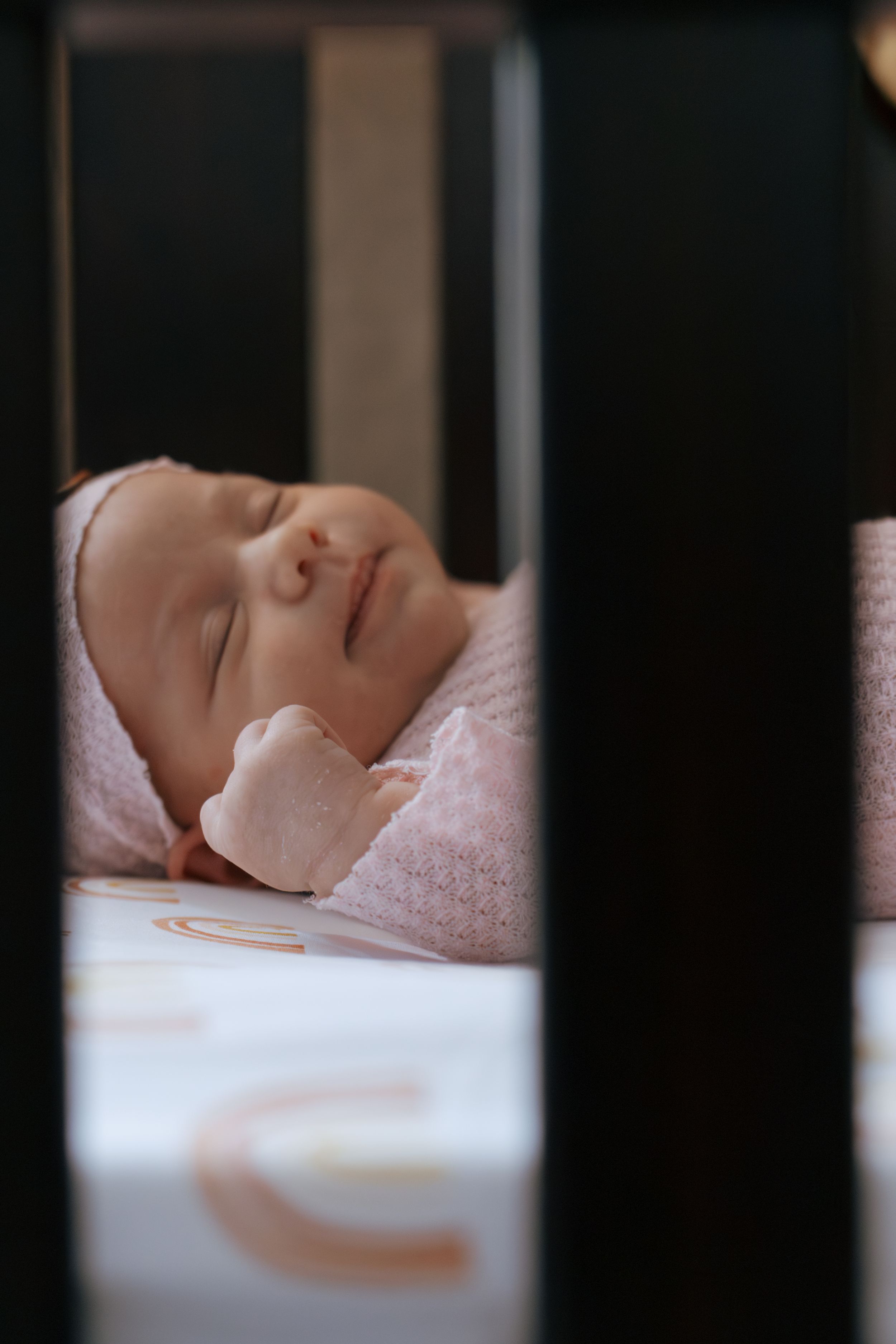 Serene baby resting in crib viewed through dark wooden bars.