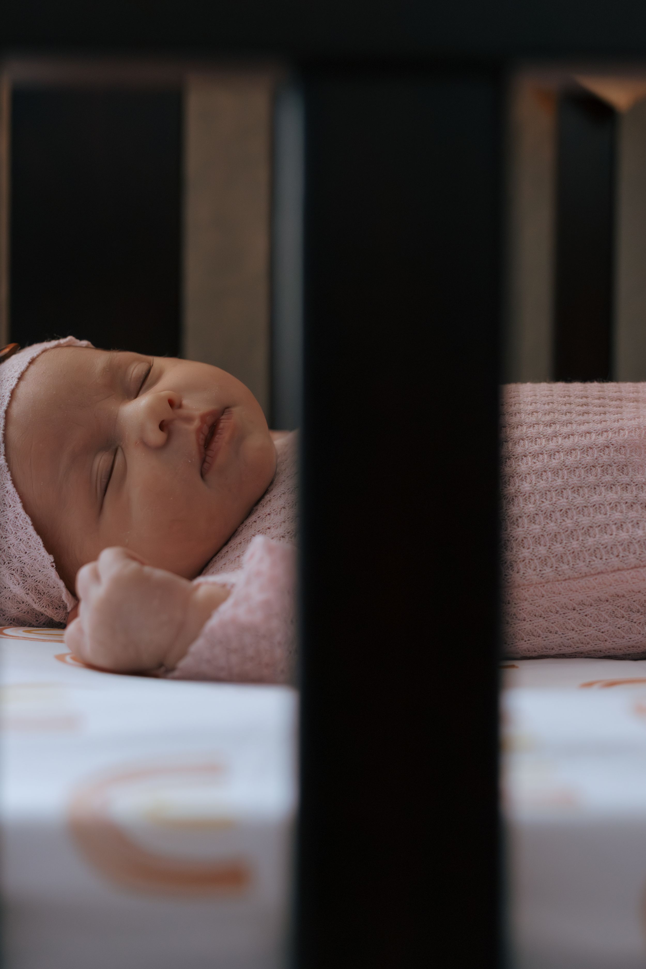 Peaceful sleeping baby viewed through crib slats in dim lighting.