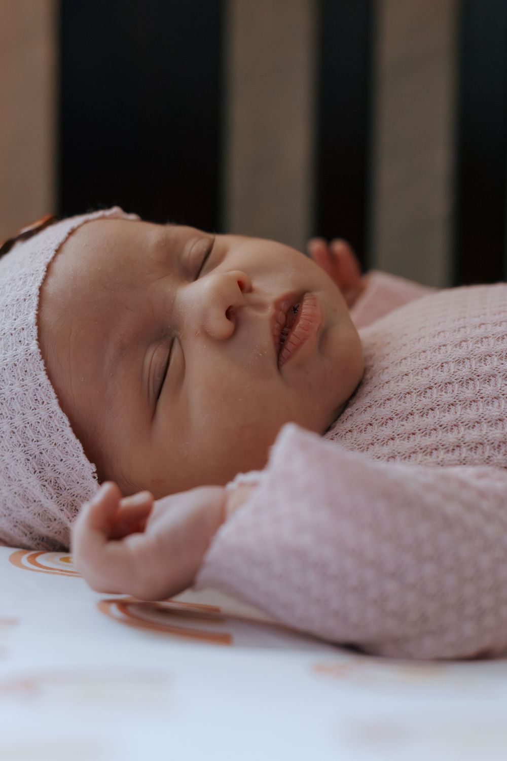 Sleeping infant in pink knit clothing photographed through crib rails.