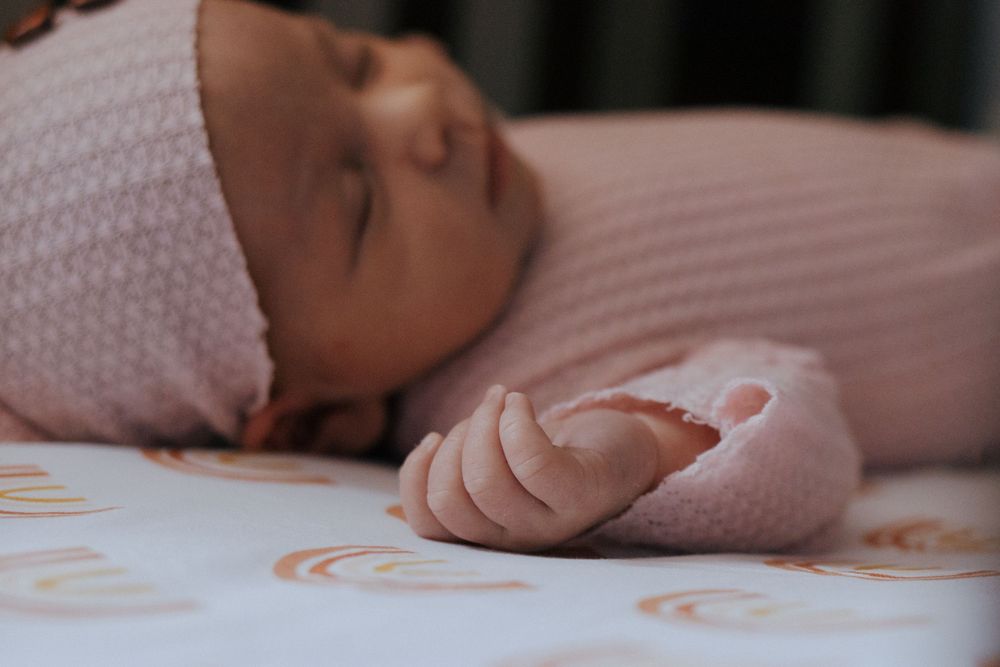 Sleeping infant in pink knit sweater lying on white surface with orange curved pattern designs.