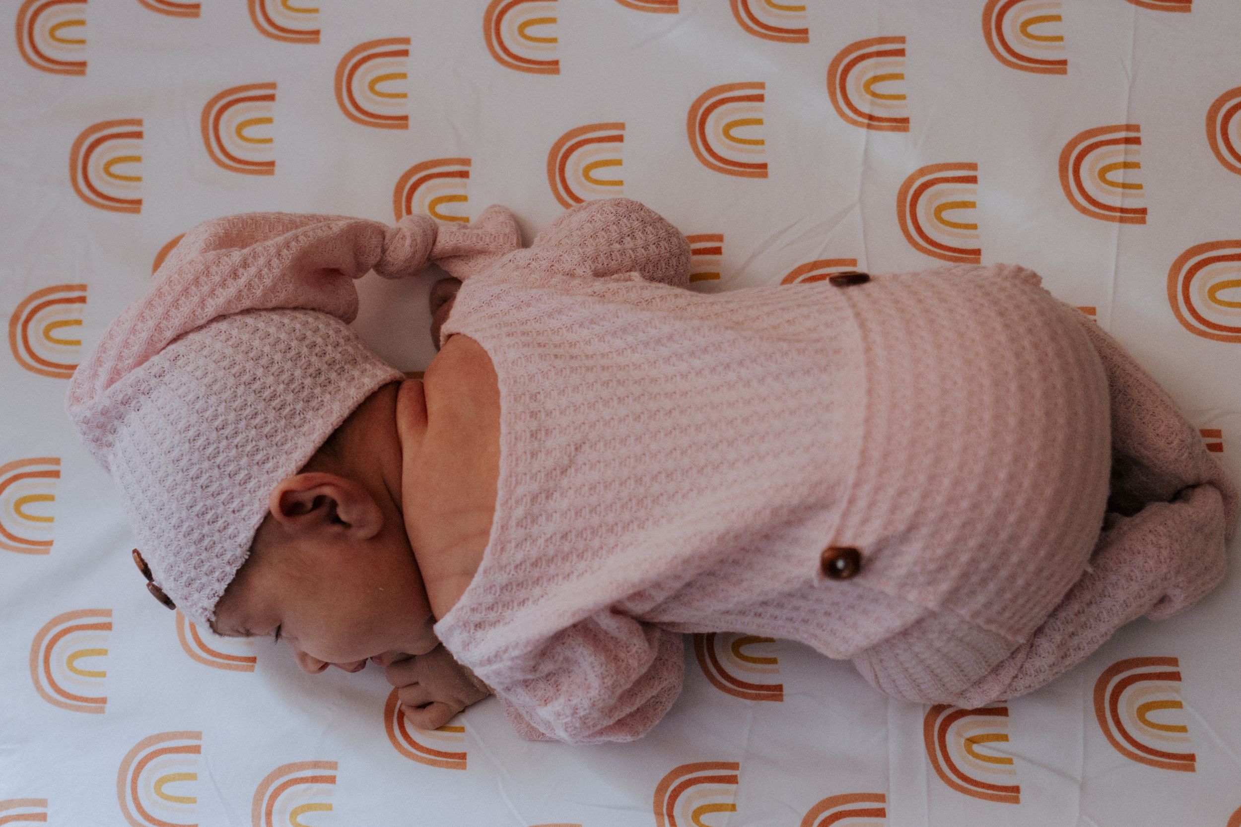 Infant in soft pink sweater lying on white surface with repeating orange curved patterns.