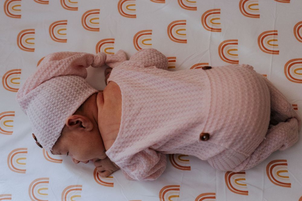 Infant in soft pink sweater lying on white surface with repeating orange curved patterns.