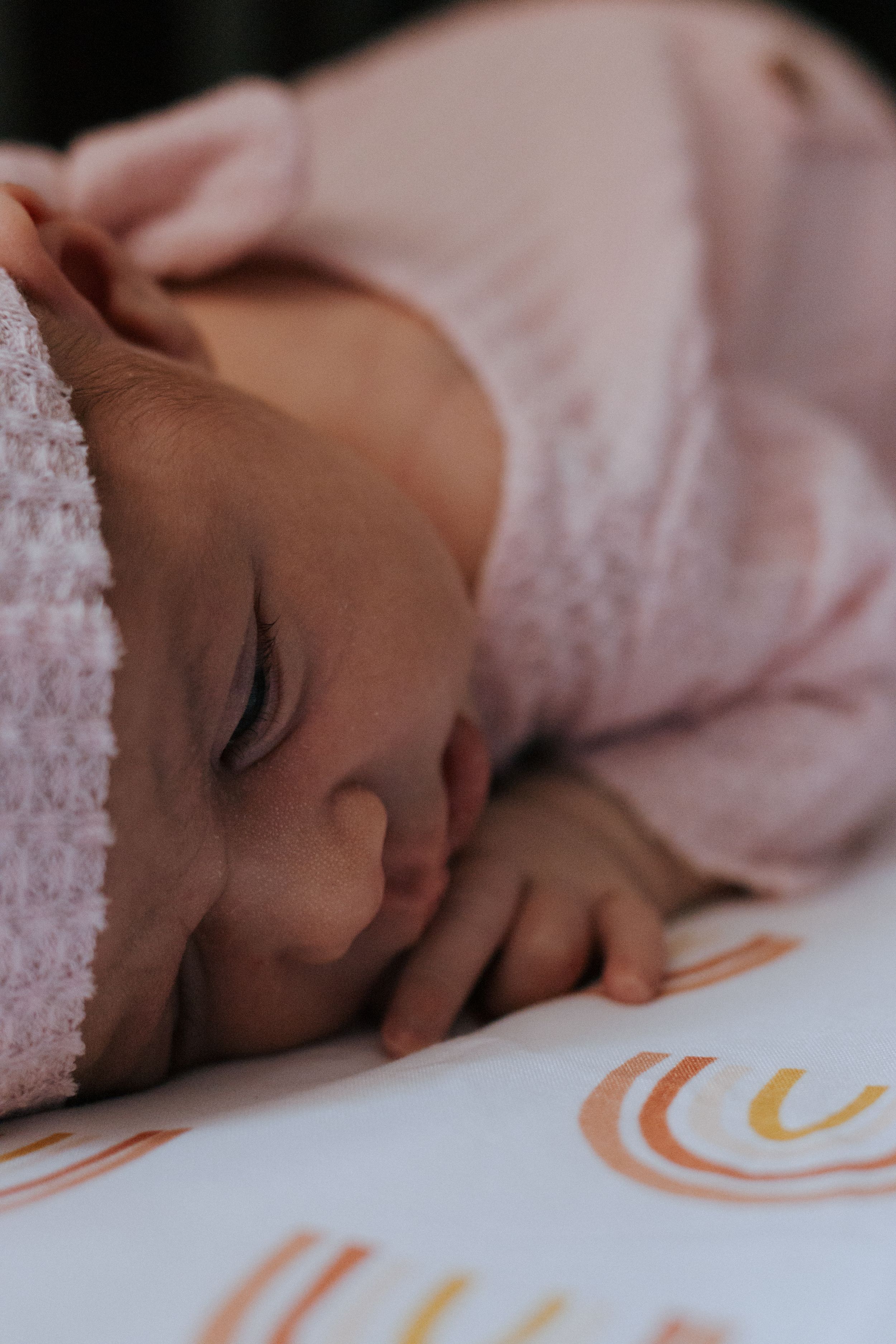 Close-up detail of baby sleeping on white surface with orange curved designs.