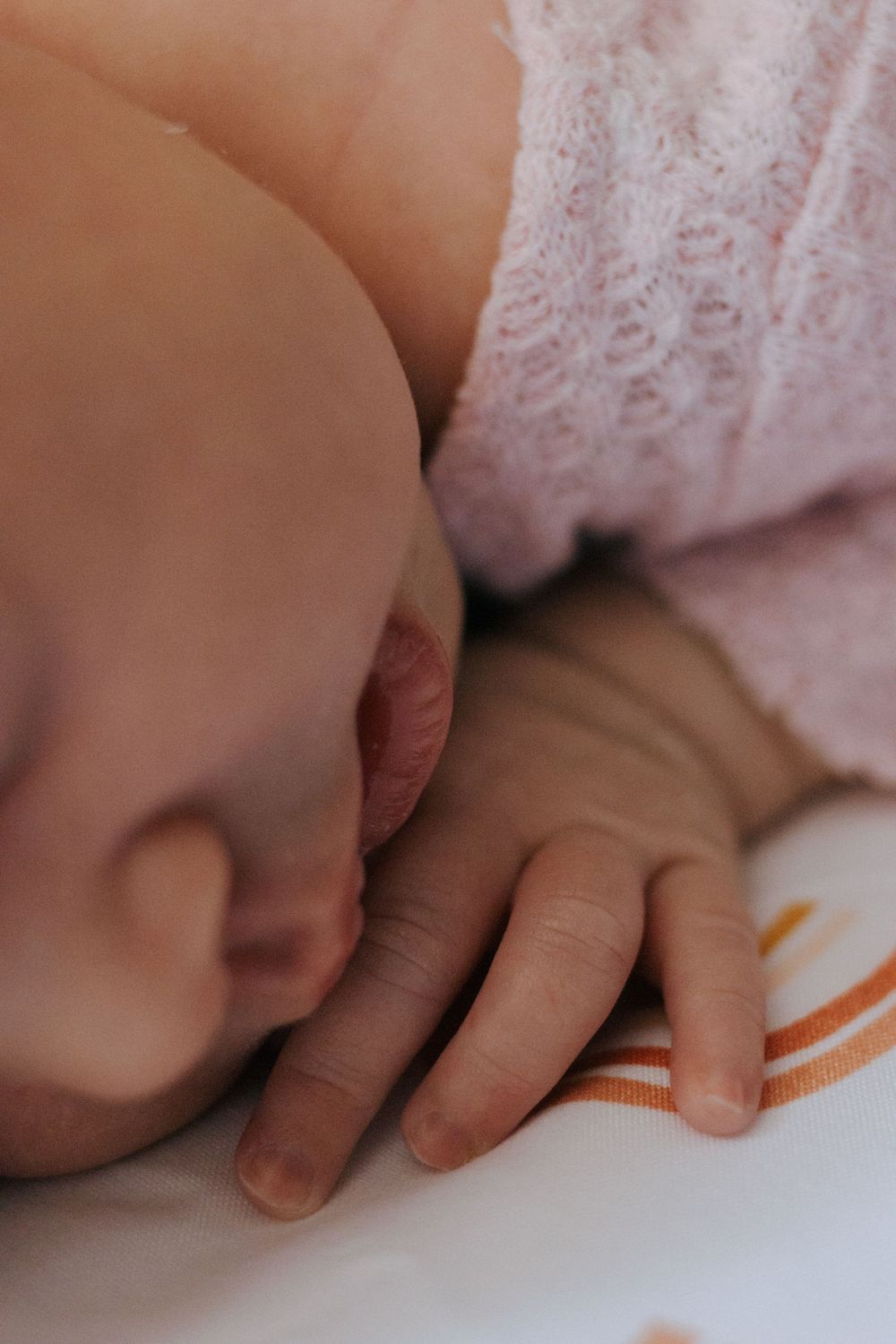 Tiny hand resting on white surface decorated with orange curved patterns.