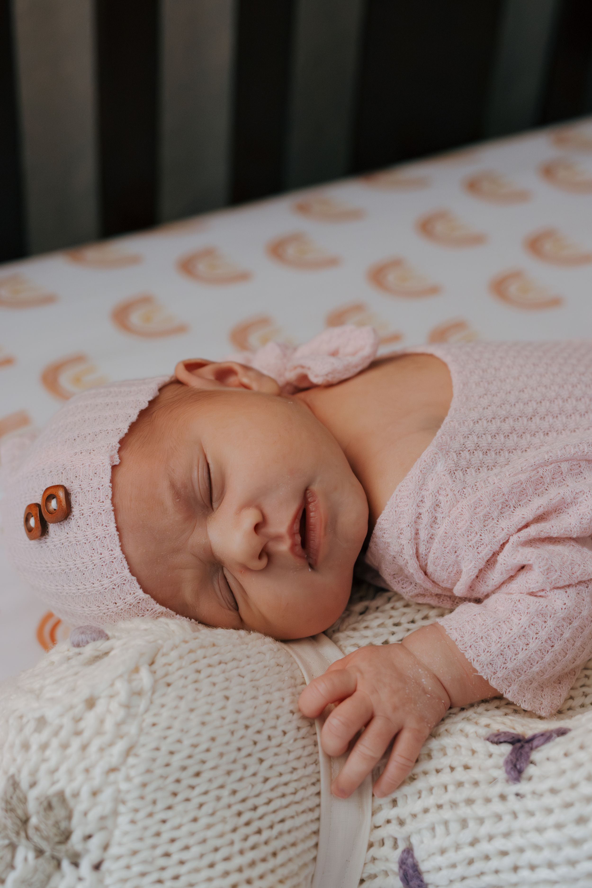 Baby sleeping peacefully on white knitted blanket wearing pink knit sweater.