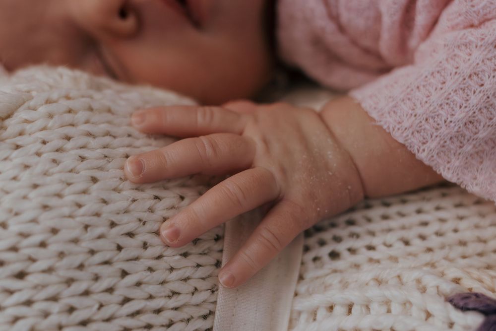 Close-up of baby's hand and torso on white knitted blanket surface.