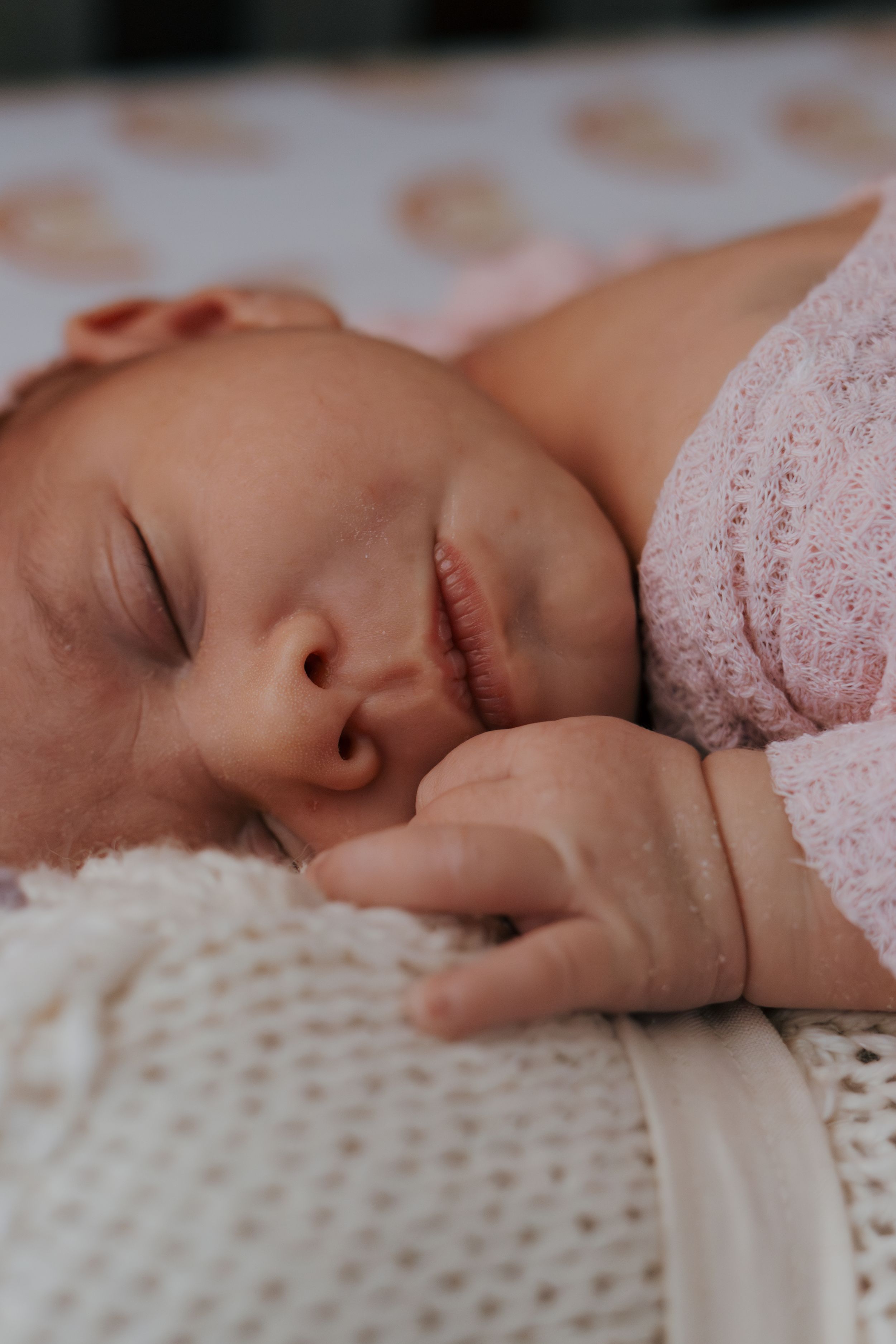 Side view of sleeping baby on white knitted blanket wearing soft pink sweater.