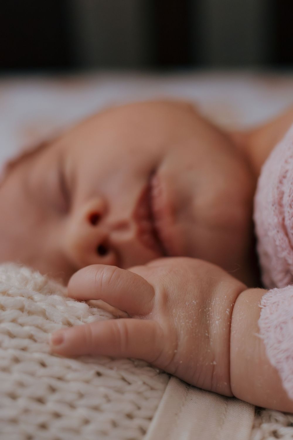 Close-up view of sleeping infant's hand resting on knitted white blanket.