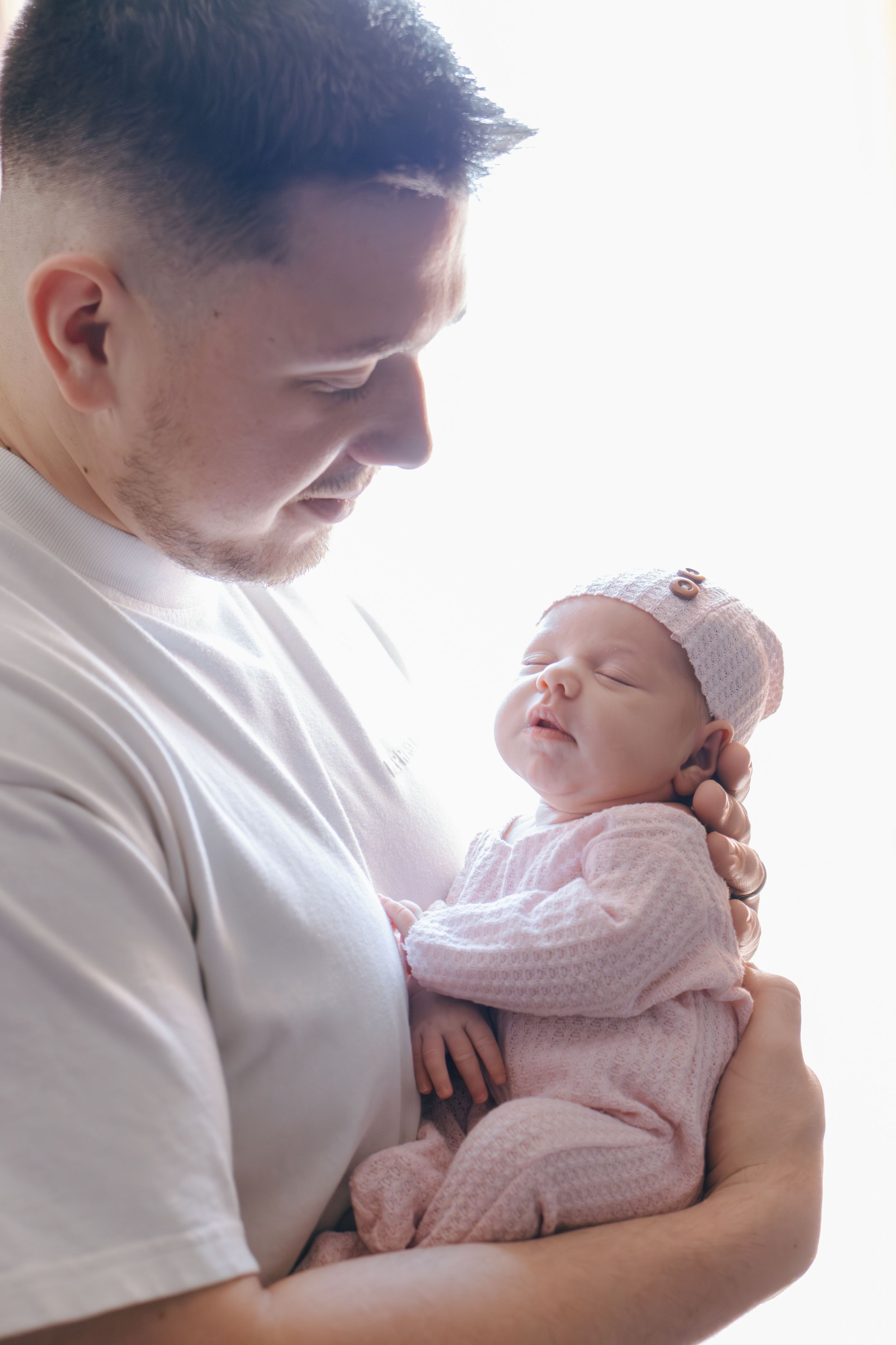 A tender moment as a newborn baby in pink sleeps peacefully against someone wearing white.