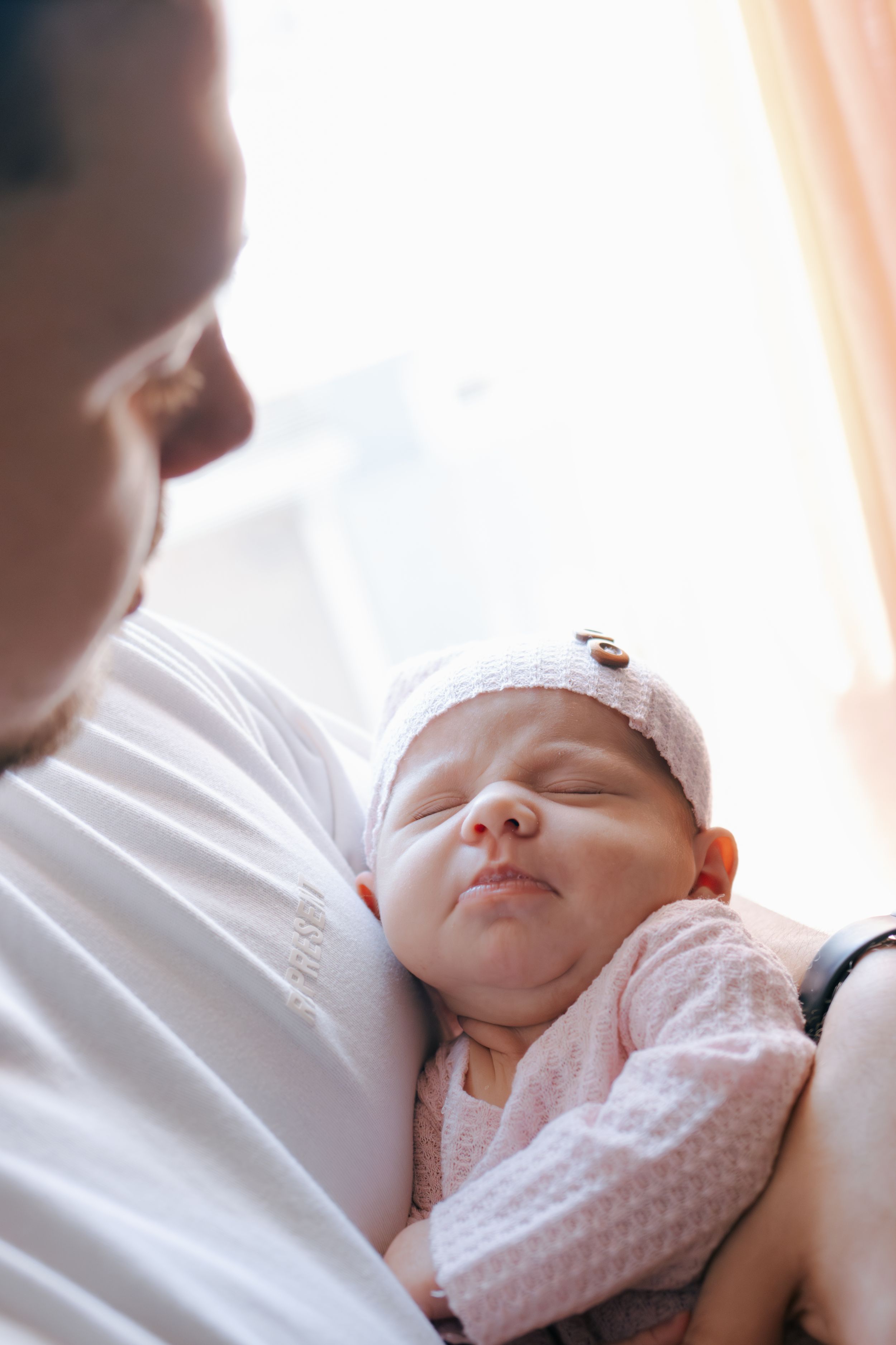 Sleeping infant in pink clothing rests contentedly against a caregiver wearing white.