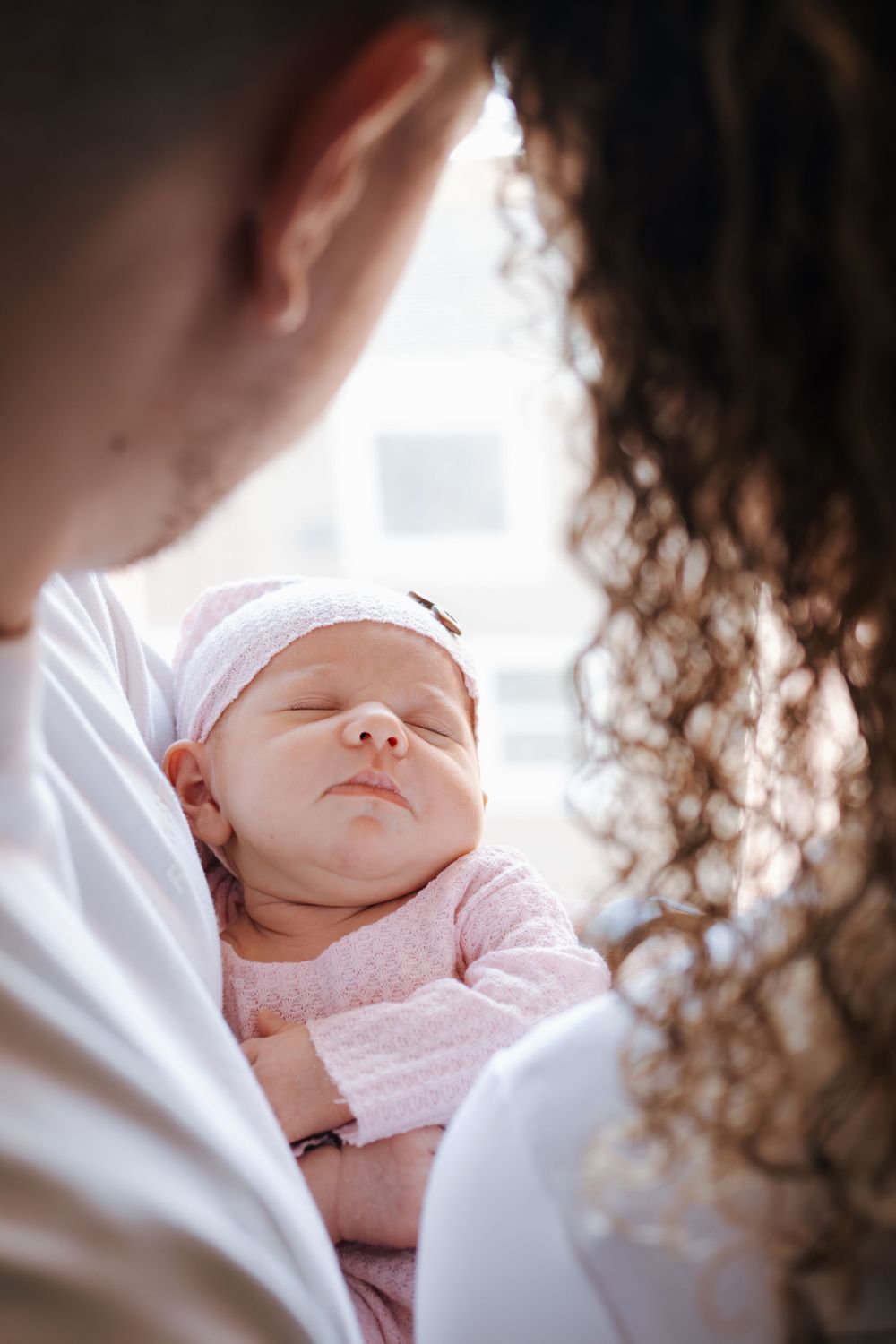 Intimate portrait of a sleeping baby in soft pink clothing being held close.