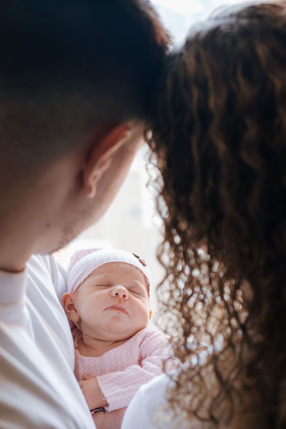 Gentle moment captured of a sleeping newborn being held near a window.