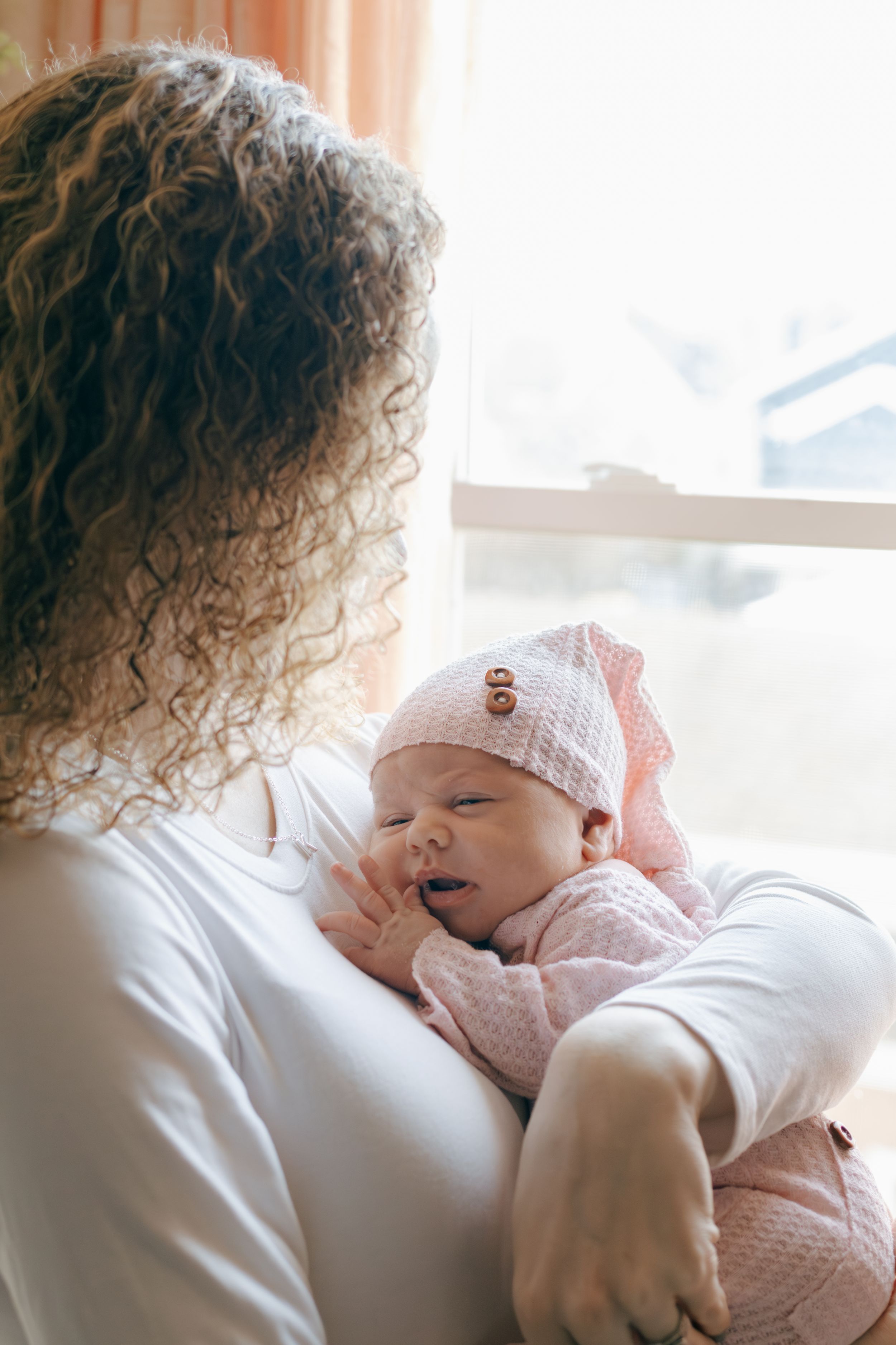 Tender moment as baby in pink clothing rests against caregiver with curly hair.