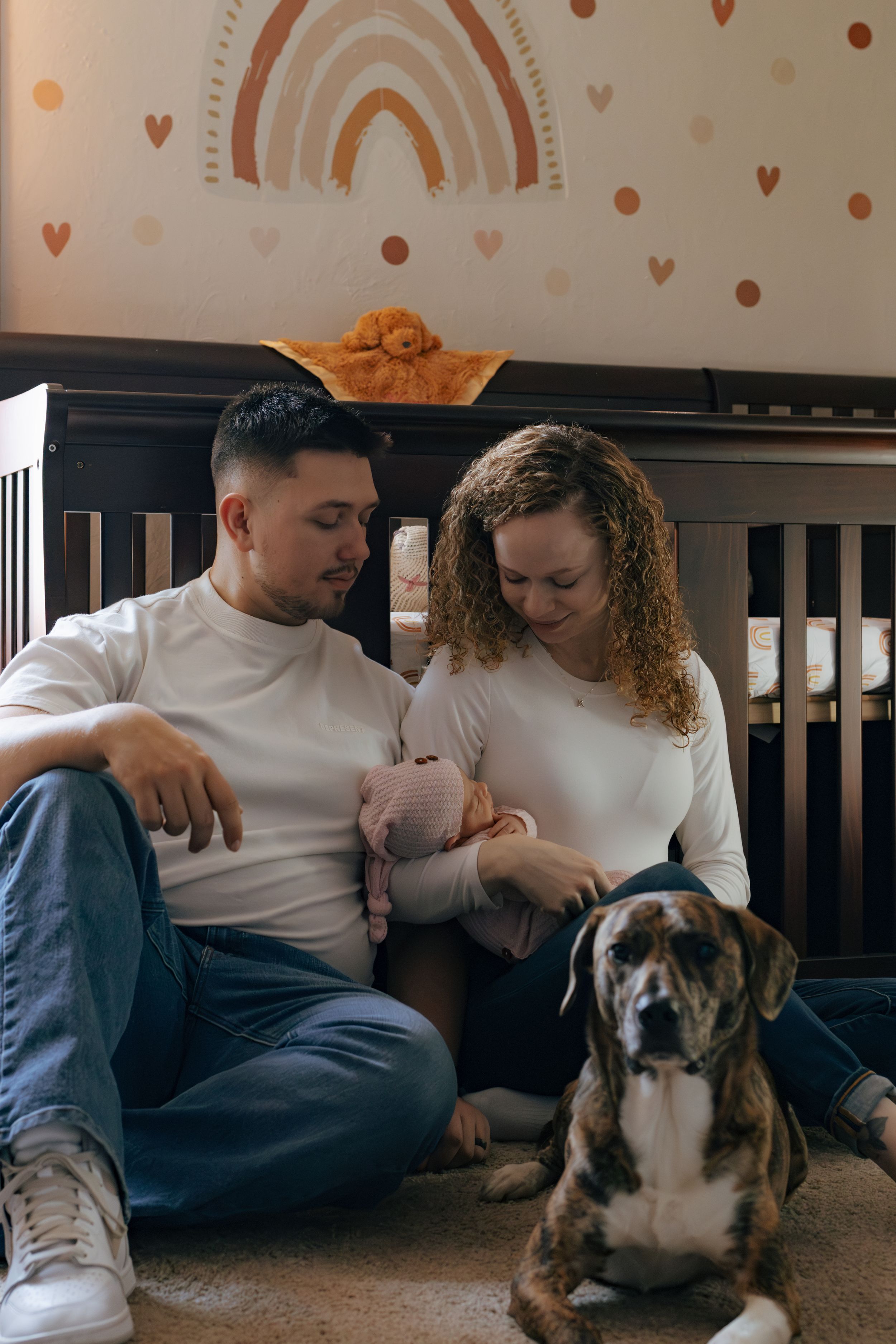 Couple in white shirts sits on floor with their boxer dog in a decorated nursery.