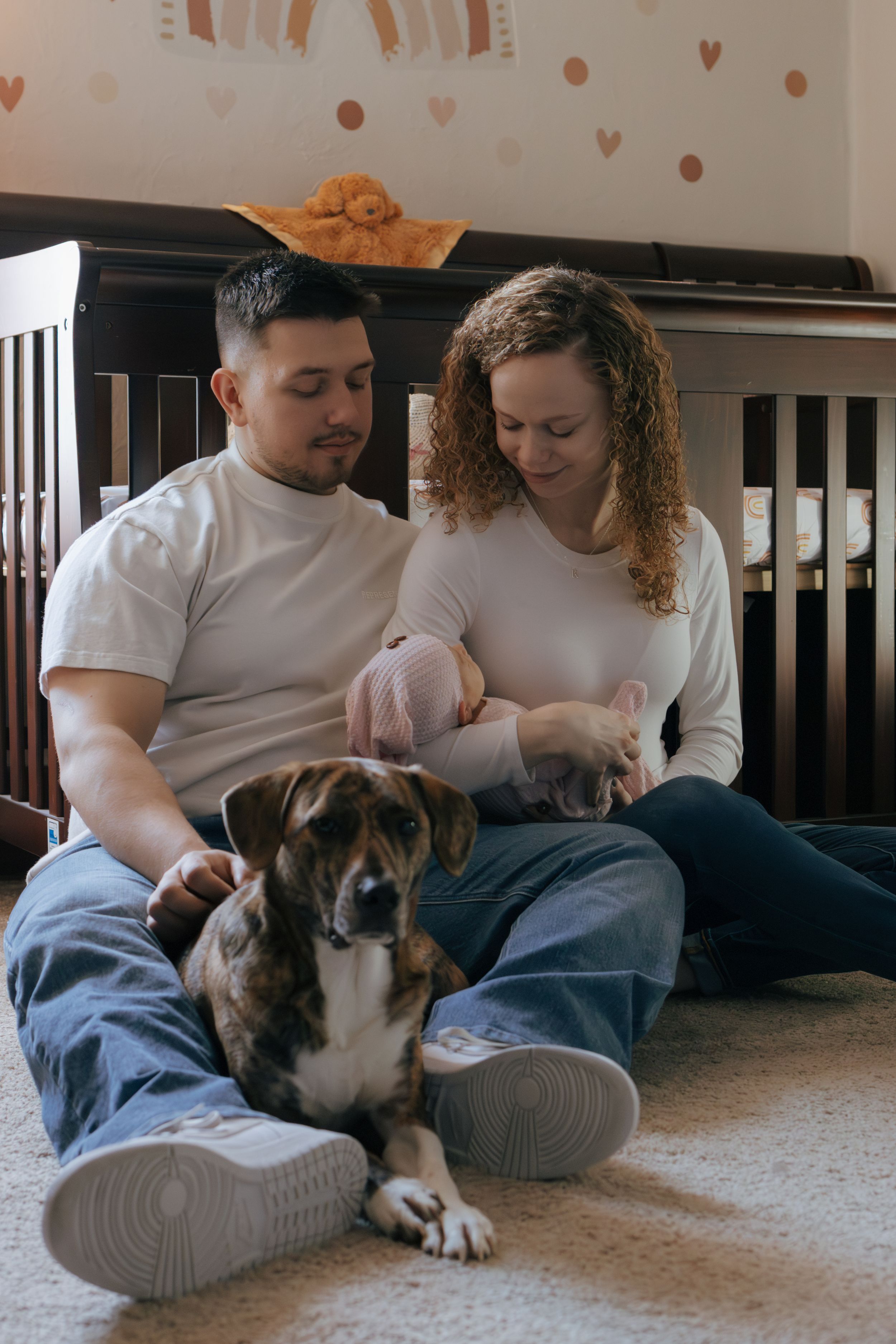 Family moment with dog as couple relaxes on carpeted floor by dark furniture.
