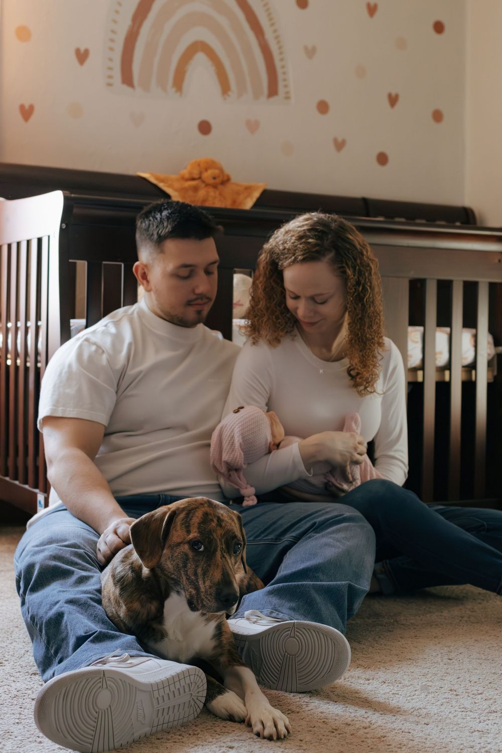 Intimate family scene with couple and their boxer dog in nursery setting.