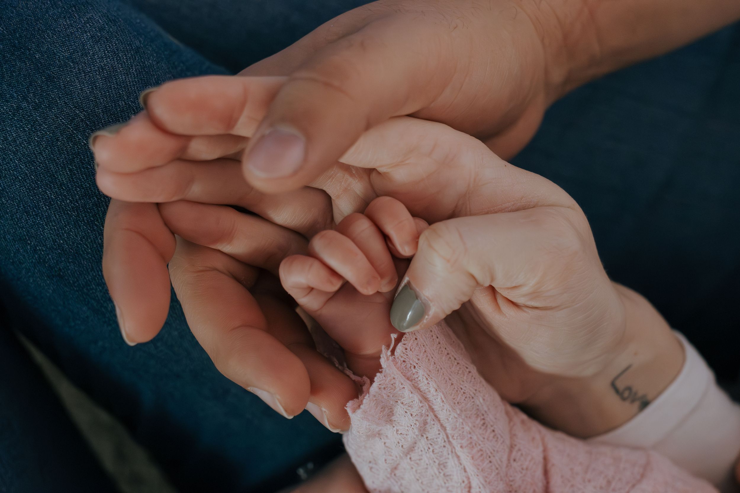 Gentle hands cradling tiny infant fingers in intimate close-up shot.