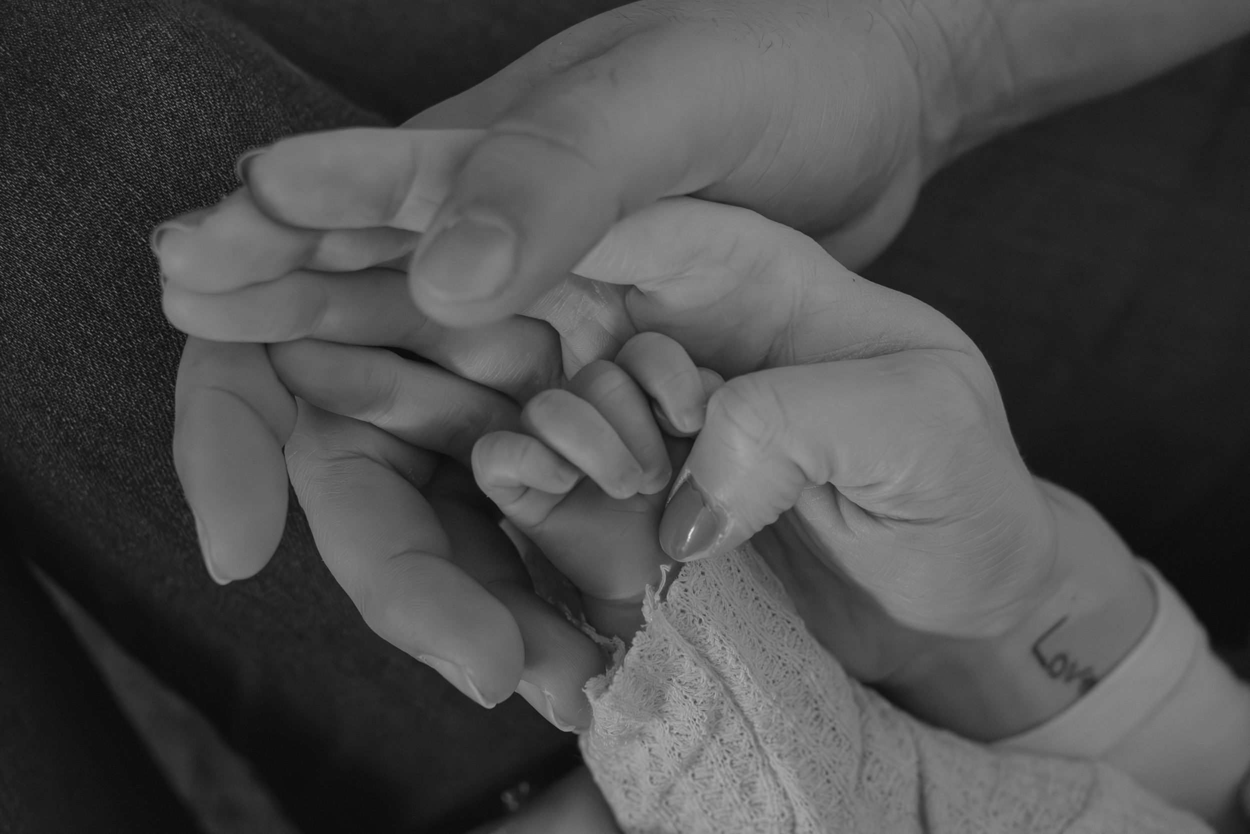 Close-up black and white photo of tiny baby fingers held in adult hands.