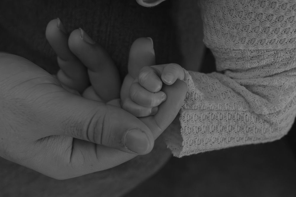 Black and white image of small baby hand being held by adult hands.