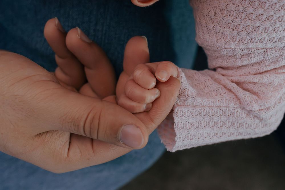 Close-up shot of tiny baby hand being held by adult fingers.