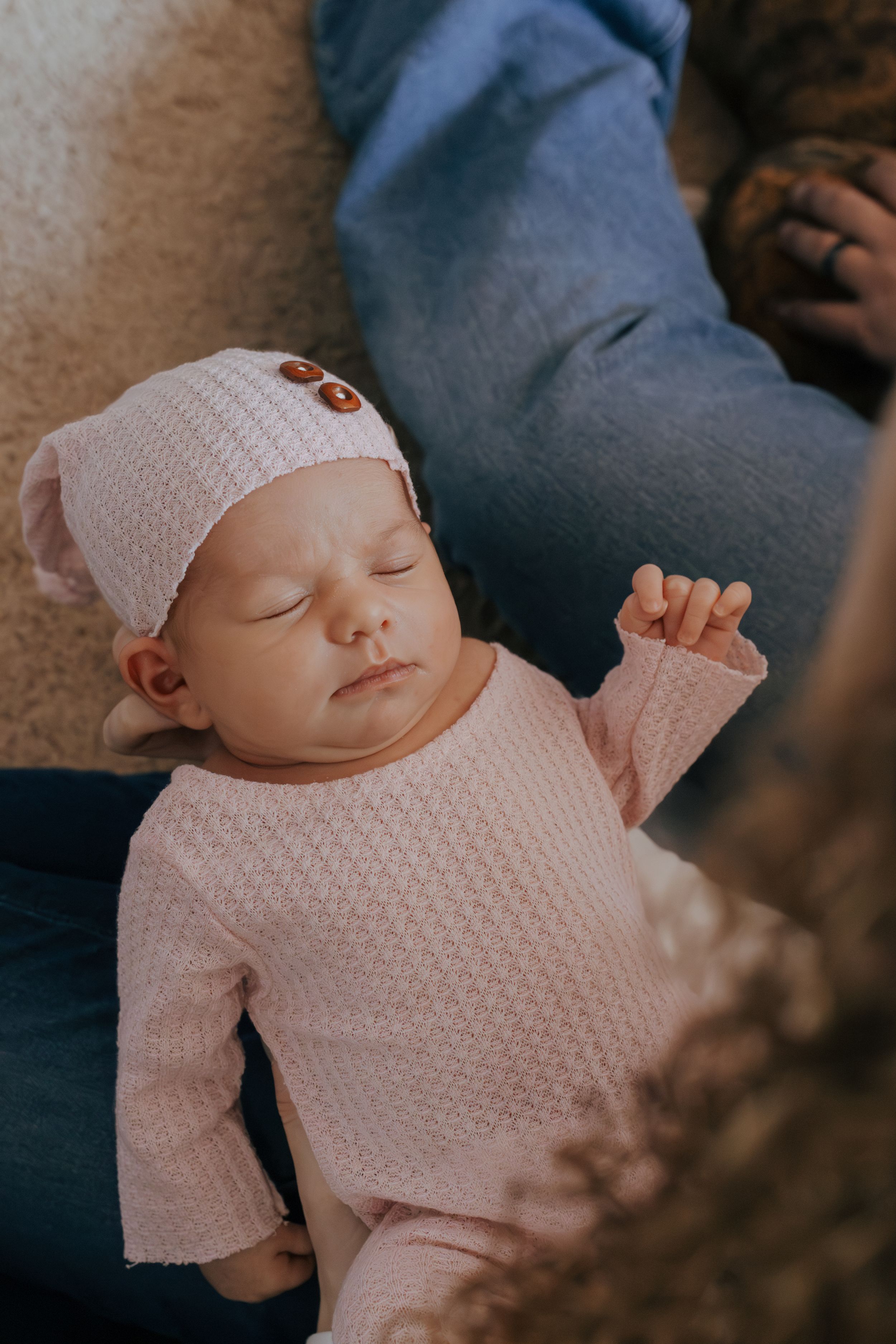 Sleeping infant wearing pink knitted clothing and hat resting on blue fabric.