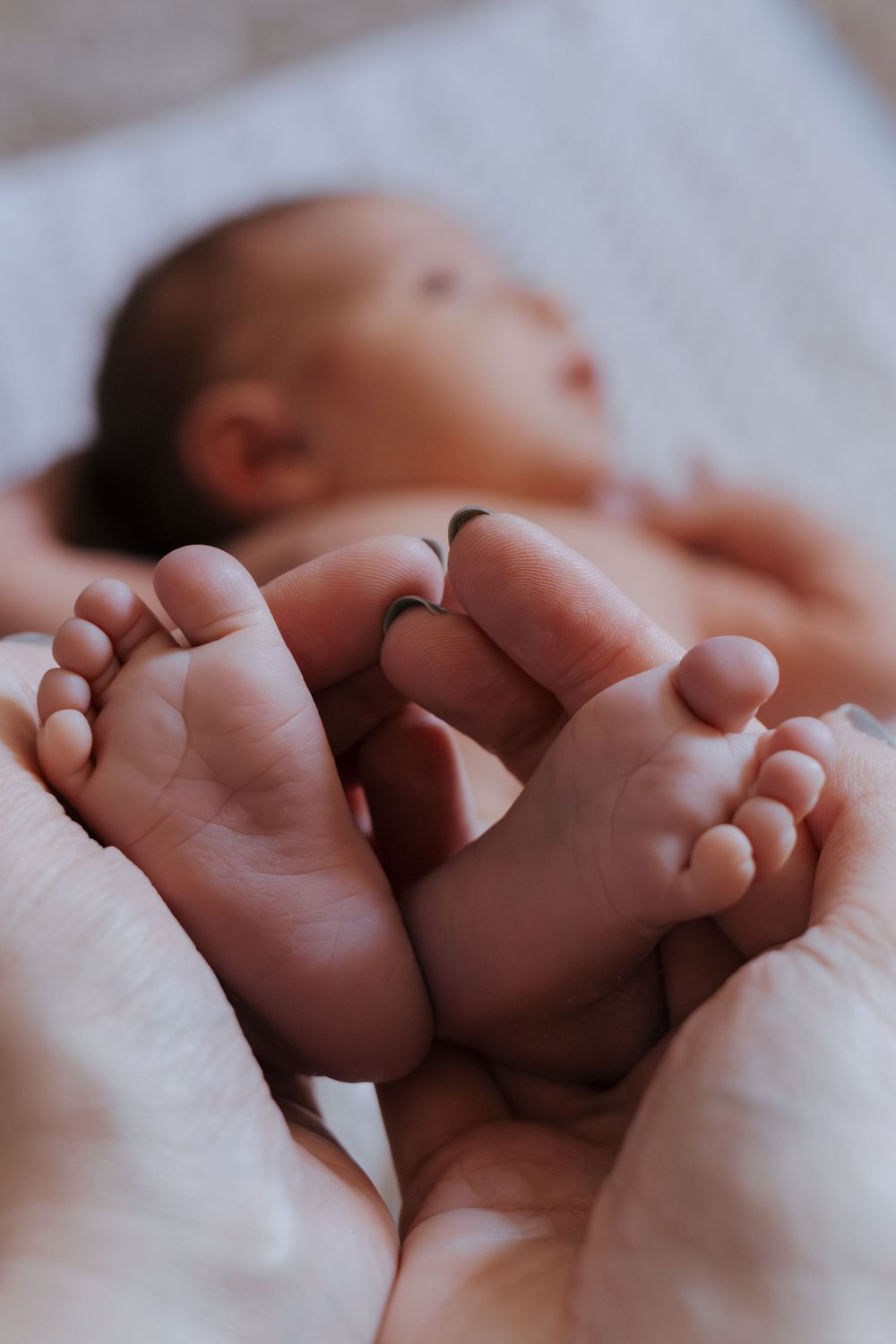 Close-up photo of newborn baby feet being held by gentle hands.
