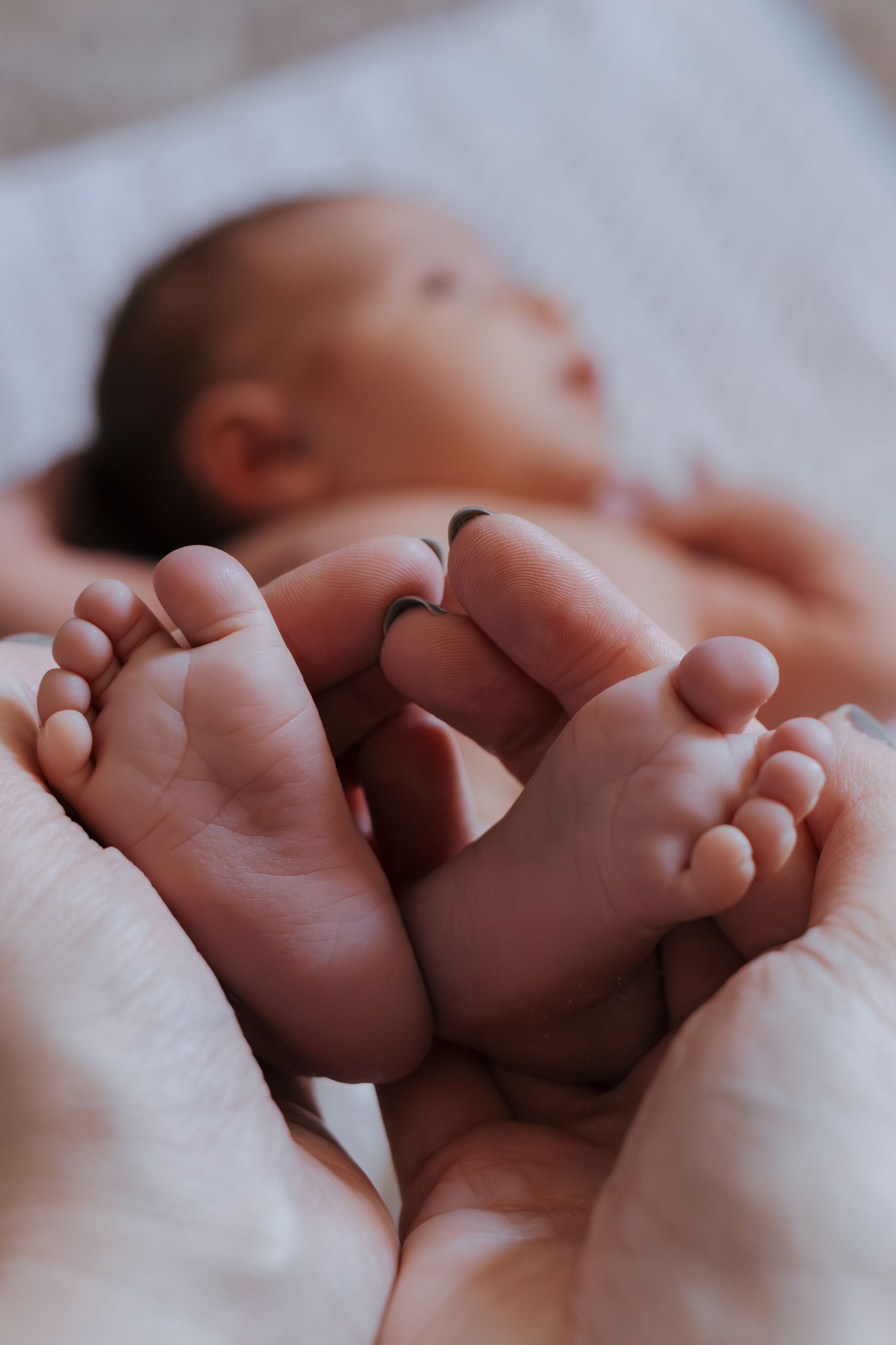 Close-up photo of newborn baby feet being held by gentle hands.