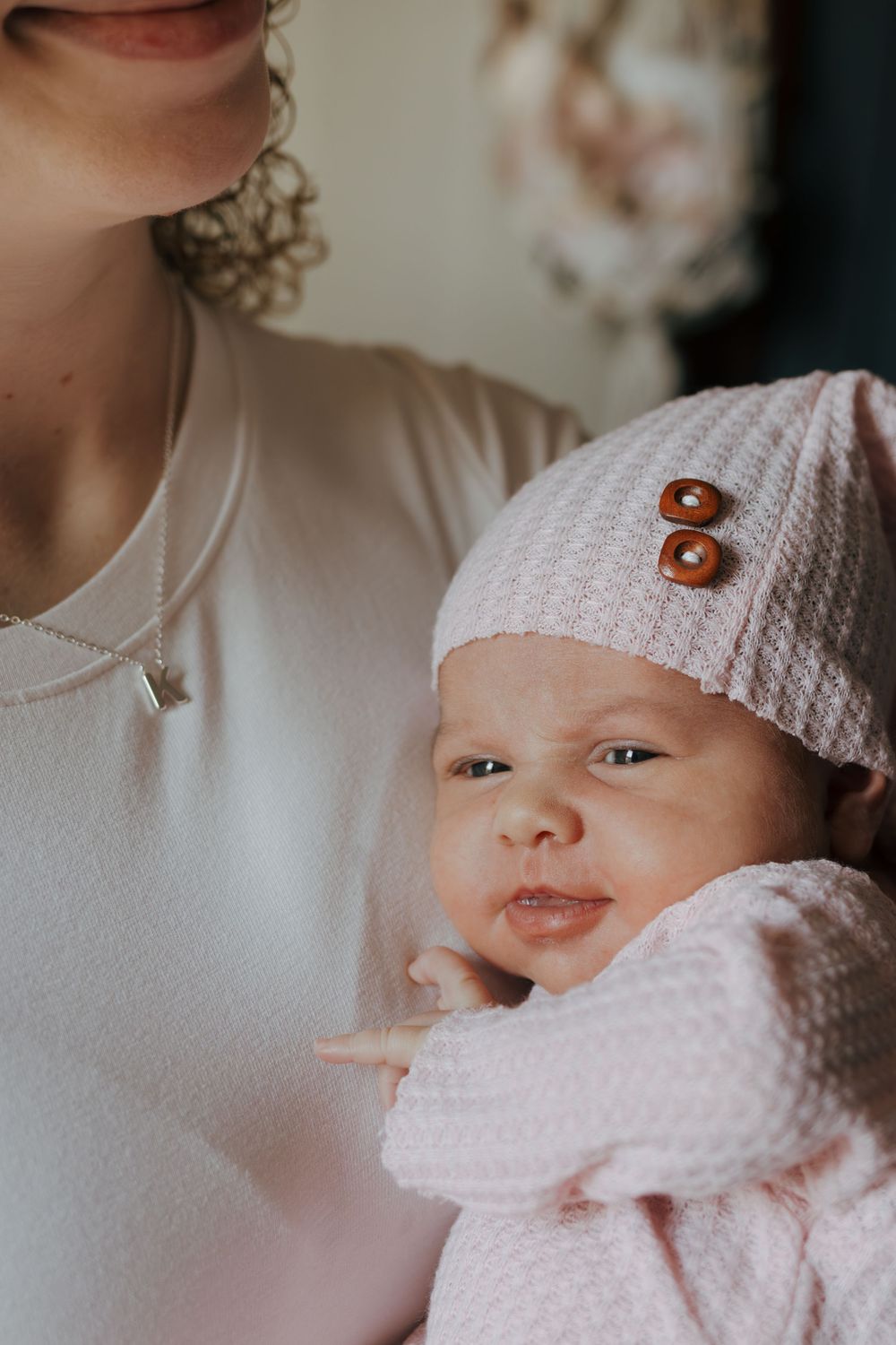 Close-up side view of baby in pink outfit and white hat with decorative button.