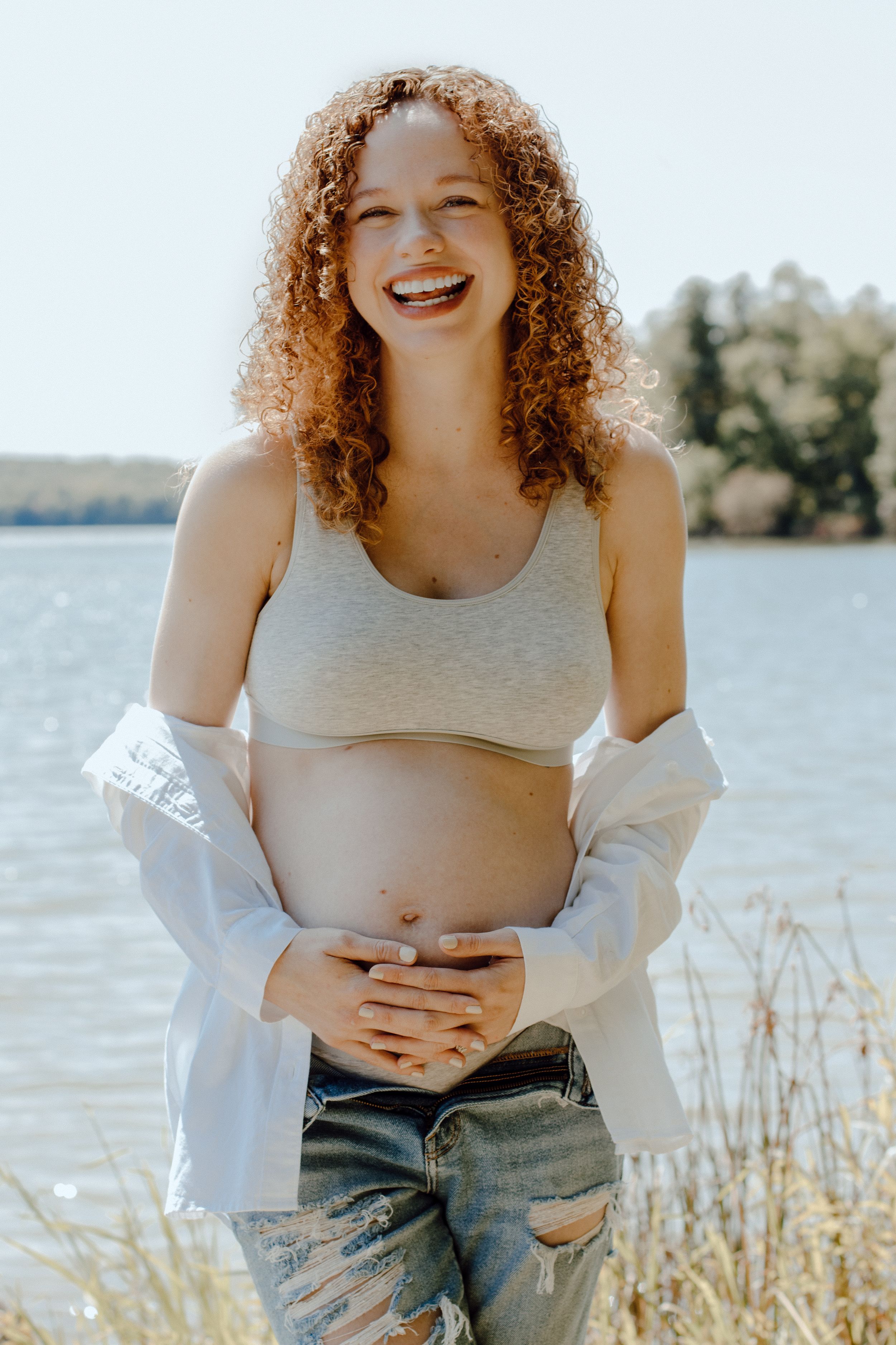 Natural outdoor maternity photos captured in bright sunlight by a lakeside setting.