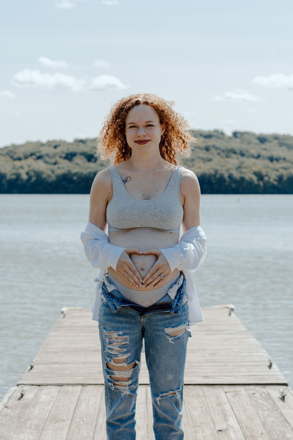 Maternity photos on wooden dock with lake and forest backdrop showing playful poses.