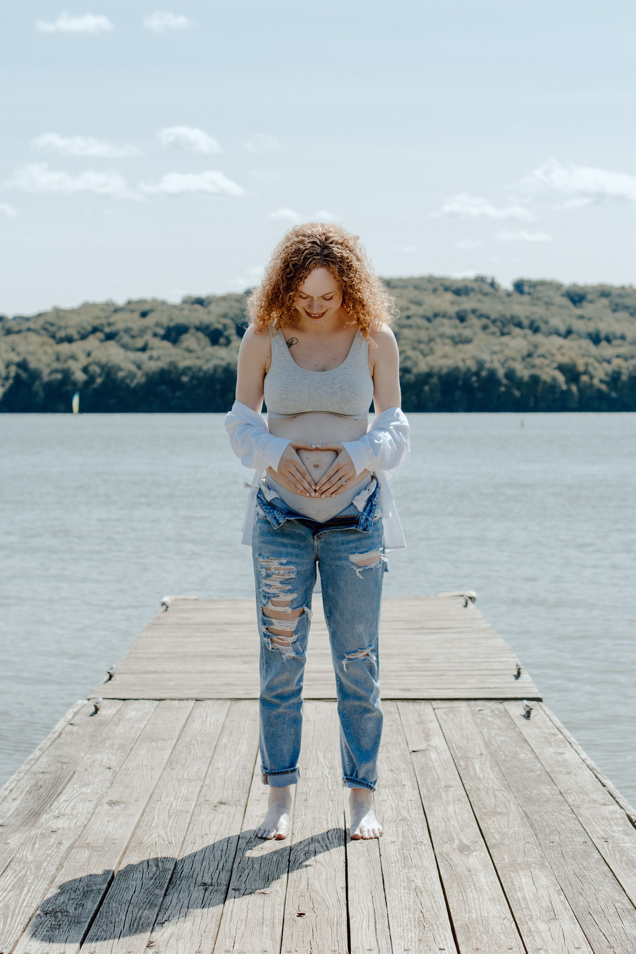 Artistic maternity photography on lakeside pier with natural lighting and scenic water views.