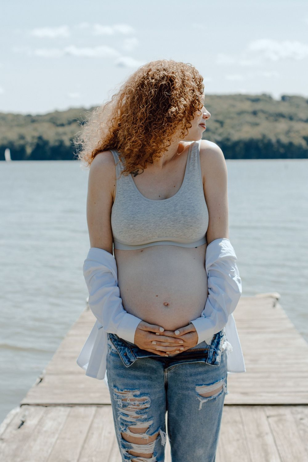 Casual pregnancy photoshoot on dock featuring distressed denim and relaxed styling.