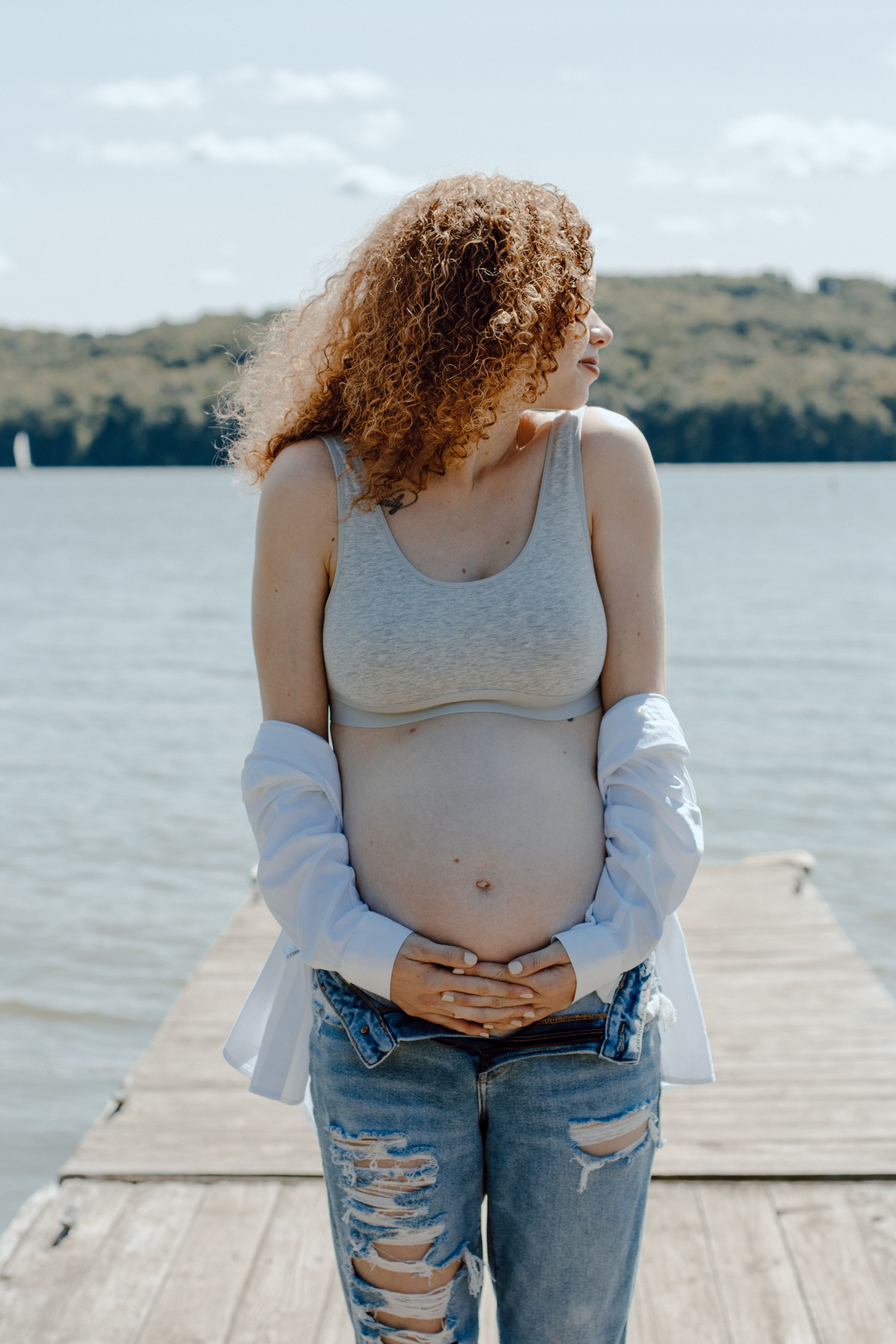 Casual pregnancy photoshoot on dock featuring distressed denim and relaxed styling.
