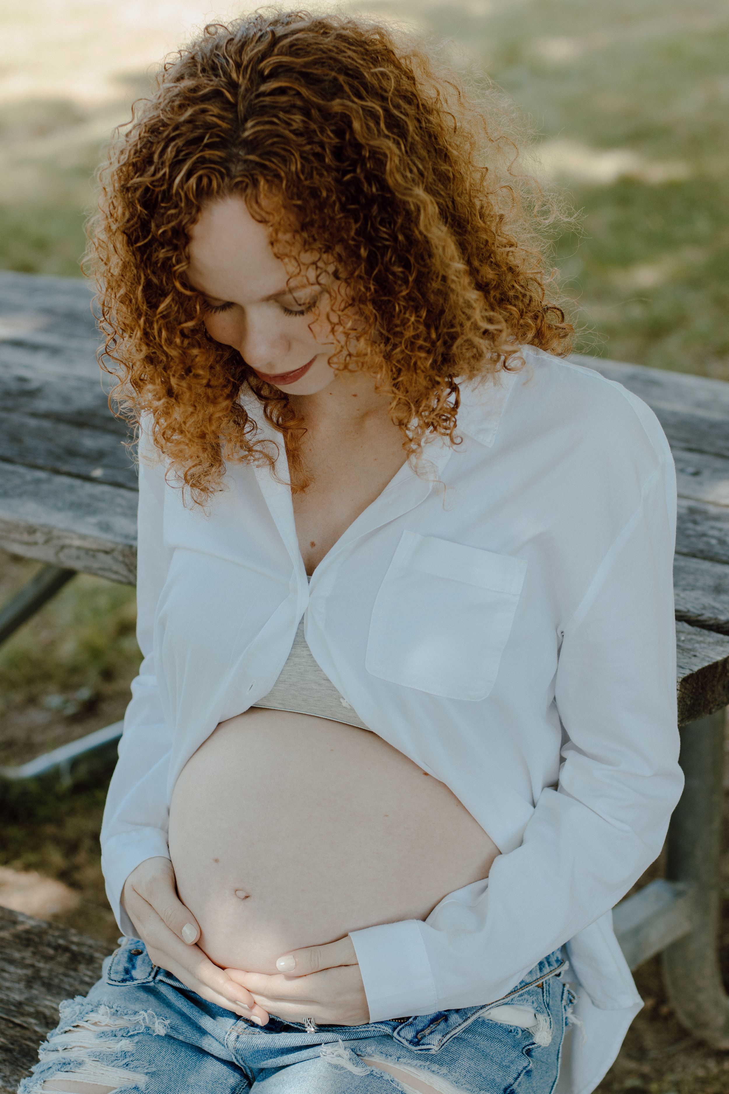 Intimate maternity portraits in white button-down shirt against natural outdoor setting.