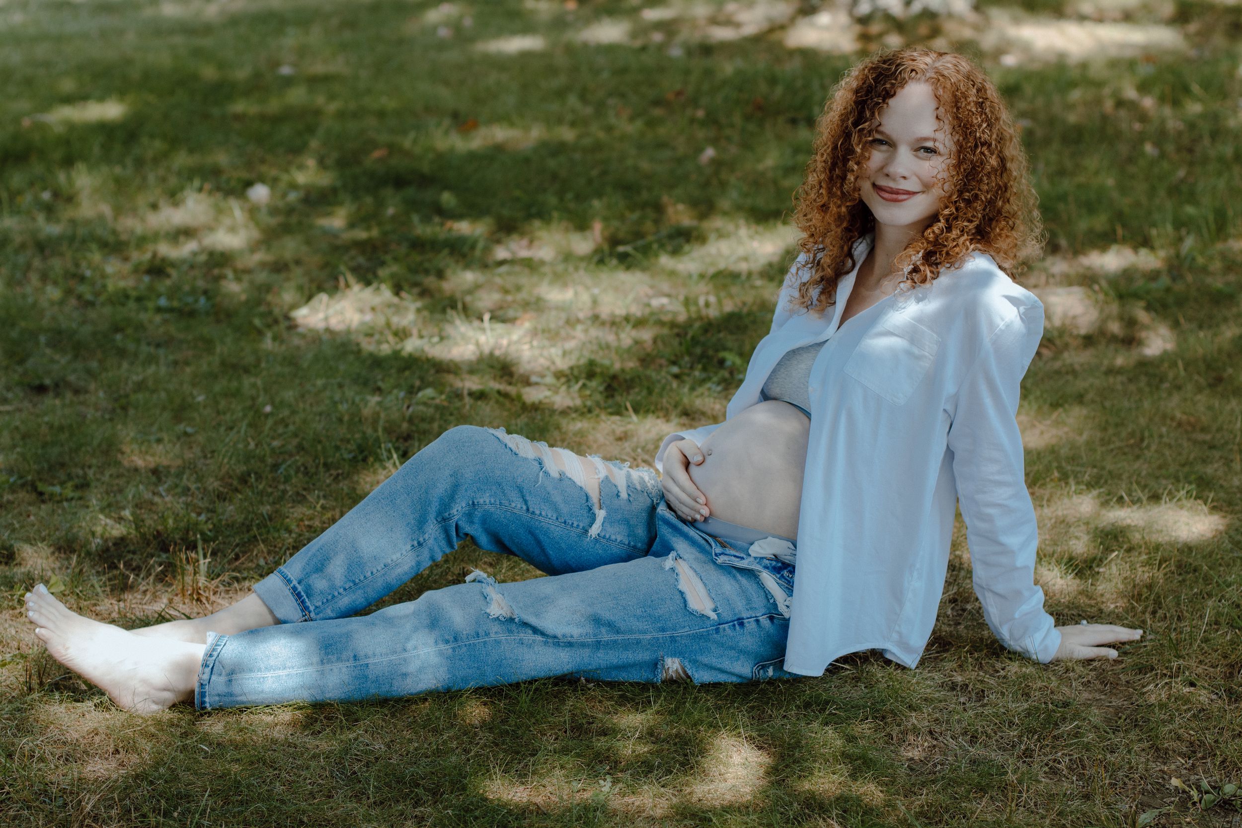 Person relaxing on grass wearing white shirt and jeans in outdoor setting.