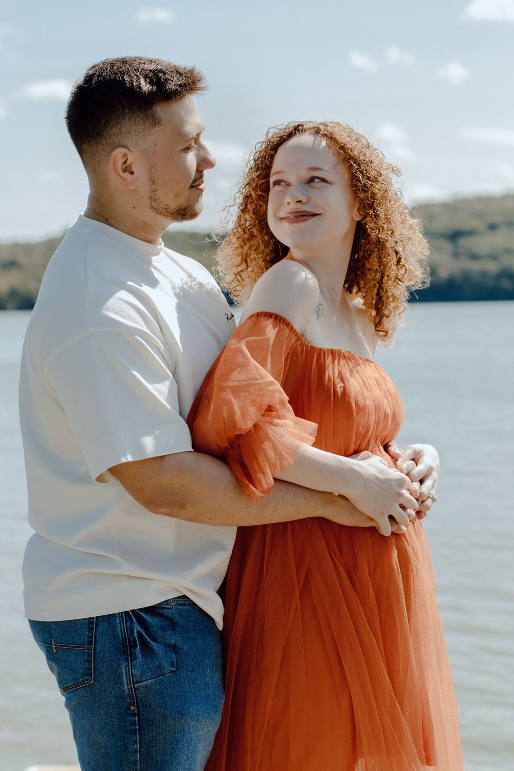 Couple in casual attire standing together on wooden dock with lake view.