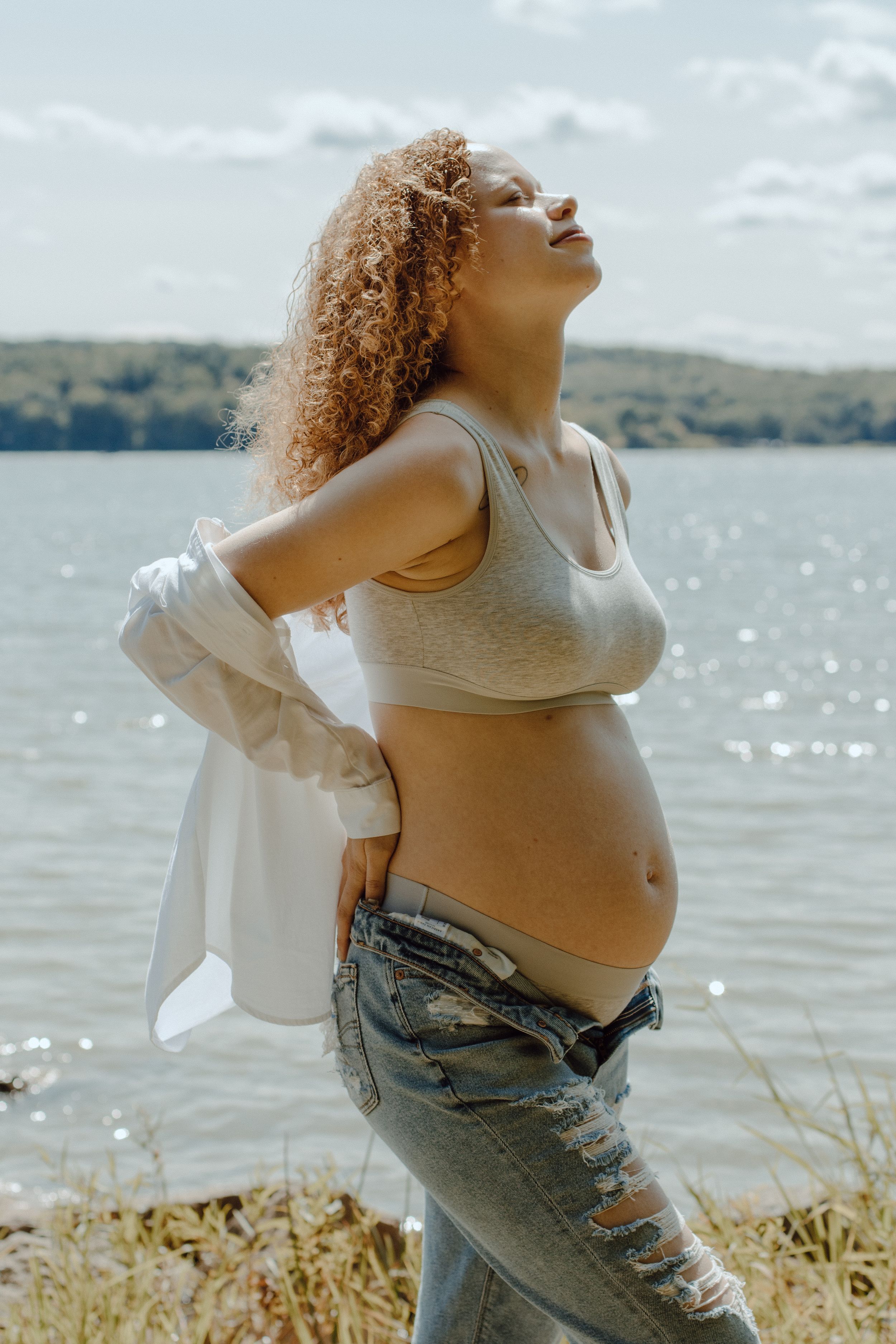 Maternity photo showing pregnant belly against sparkling lake water and natural scenery.