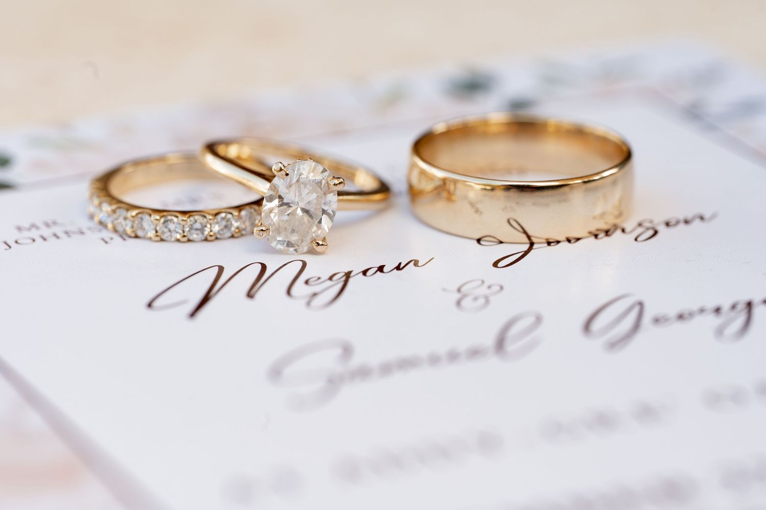 Gold wedding rings and diamond engagement ring displayed on elegant wedding invitation.
