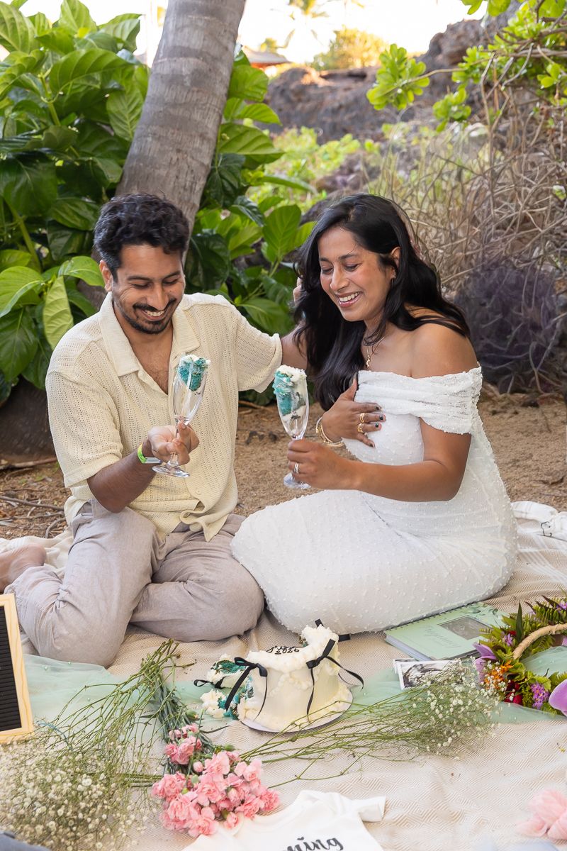A couple enjoys a romantic picnic outdoors with drinks and flowers on a sunny day.
