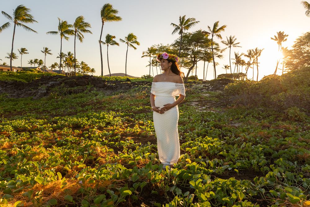 Two figures embrace on a hillside overlooking palm trees during a golden Hawaiian sunset.
