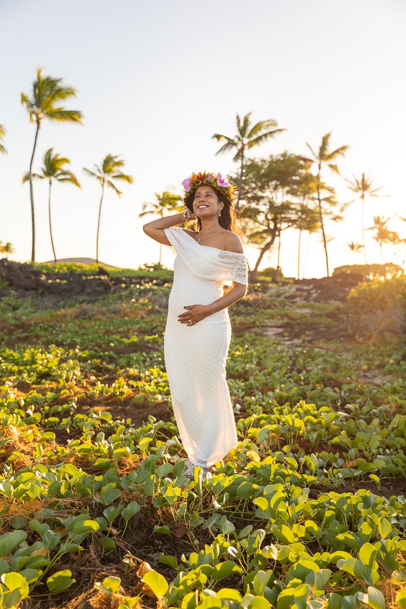 Person wrapped in white fabric dances joyfully in a lush garden field at sunset with palm trees in the background.