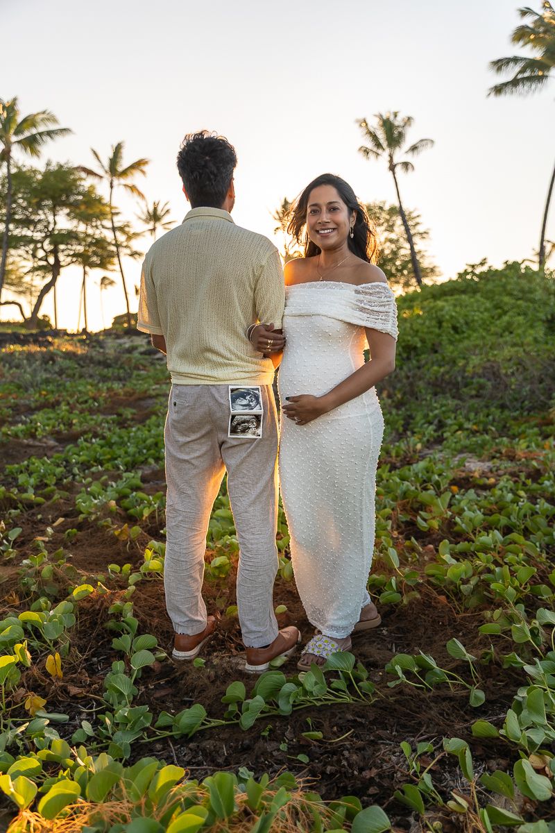 A couple poses for photos in a tropical garden setting with palm trees and lush vegetation at golden hour.