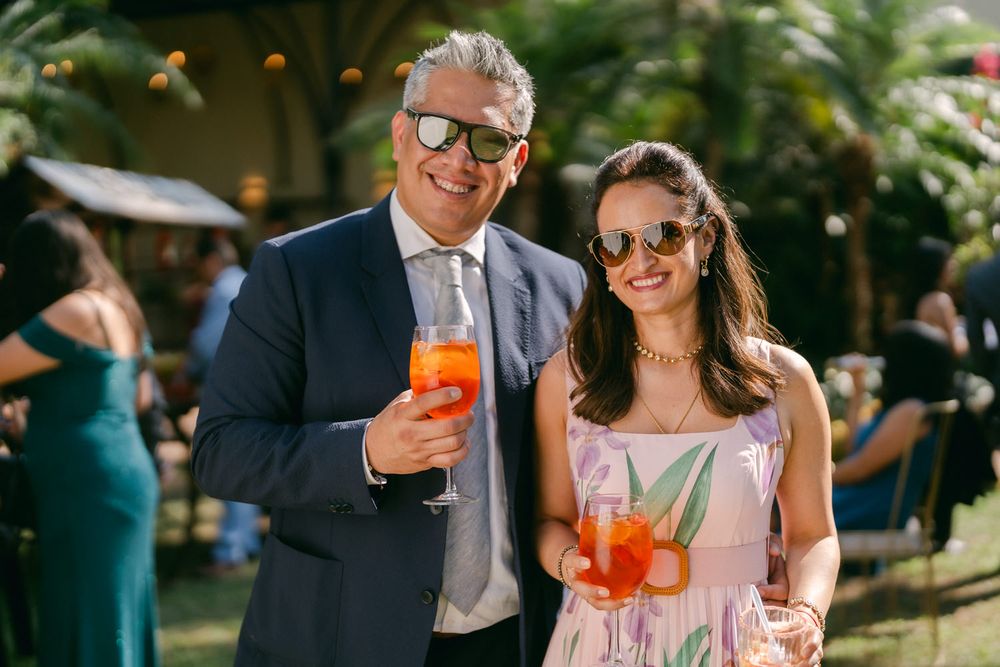 Two guests enjoy bright orange Aperol Spritz cocktails at an outdoor summer garden party.