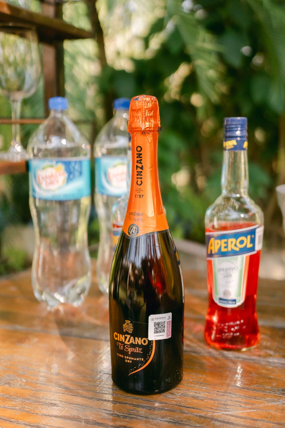 Various bottles of liquor and cocktail ingredients arranged on a rustic wooden table surface.