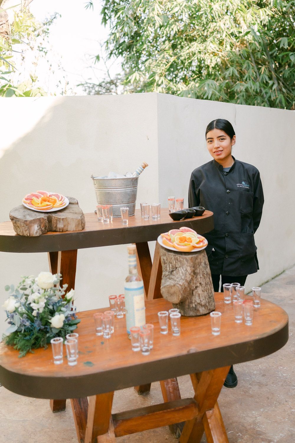A catering setup features wooden display tables with citrus fruits, glassware and a staff member in a black chef coat.