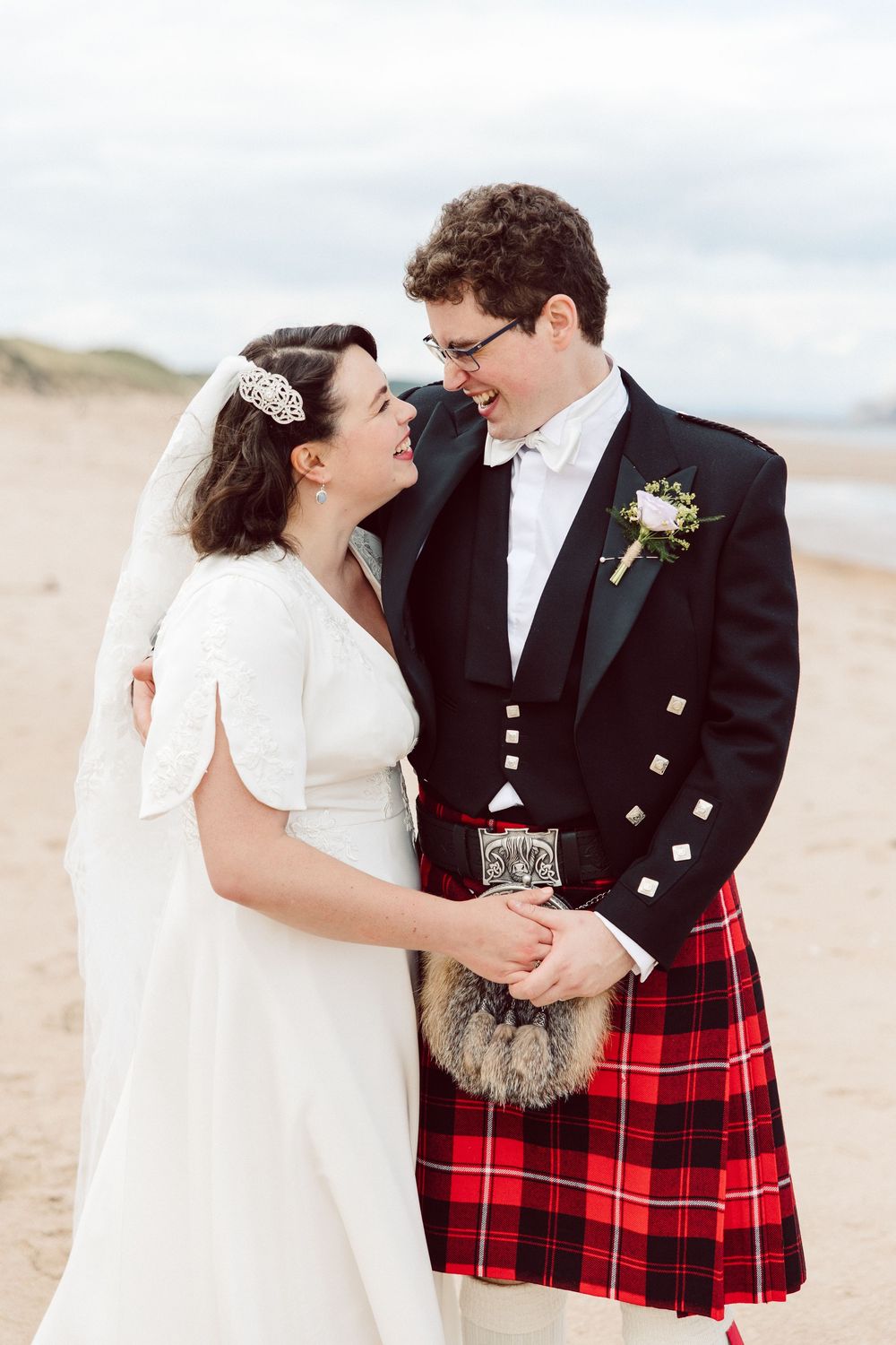 Romantic wedding couple on beach with groom wearing traditional Scottish kilt and bride in elegant white dress.
